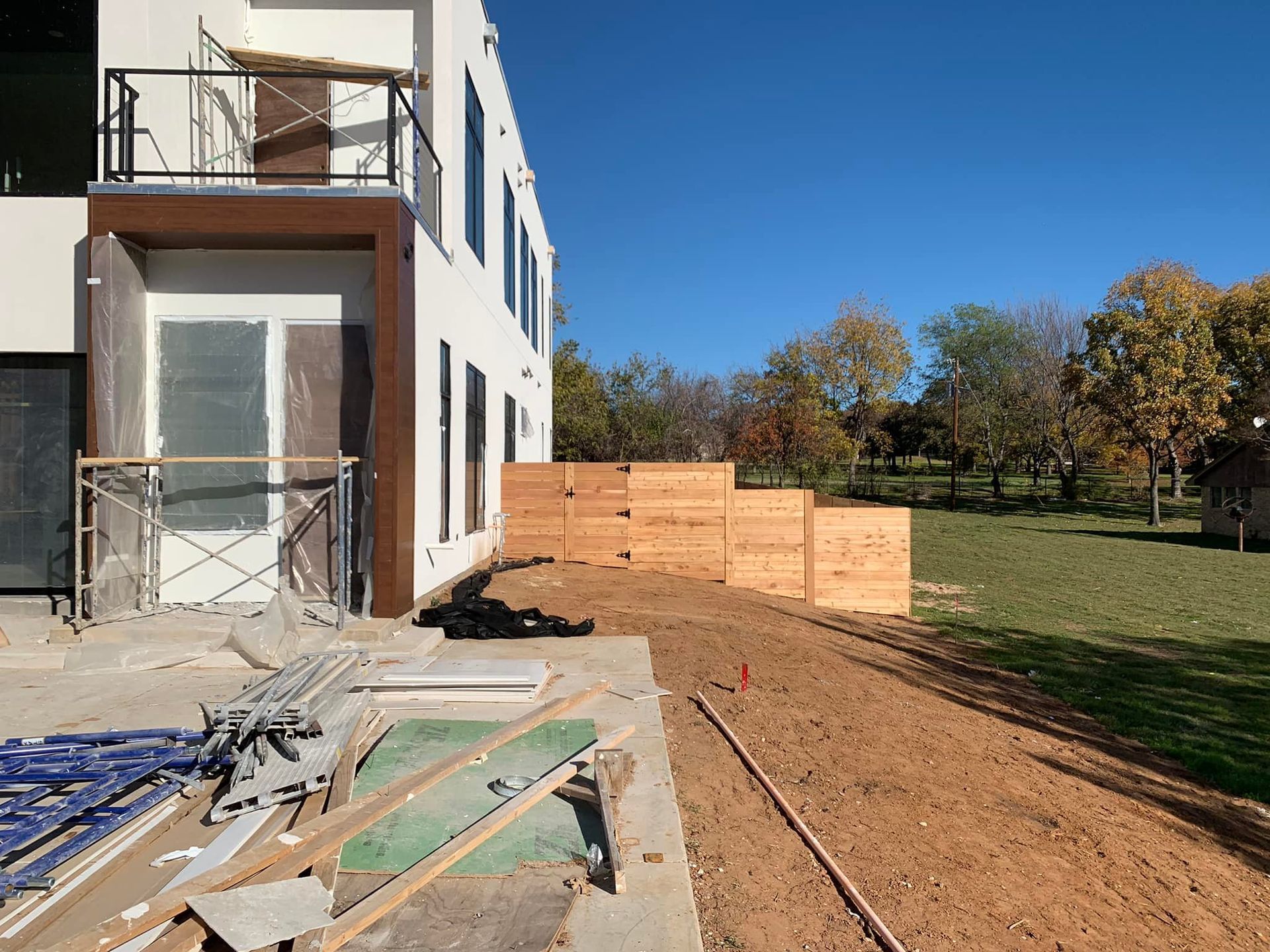 Construction site: modern building with brown trim, wooden boxes, and a dirt yard under a blue sky.