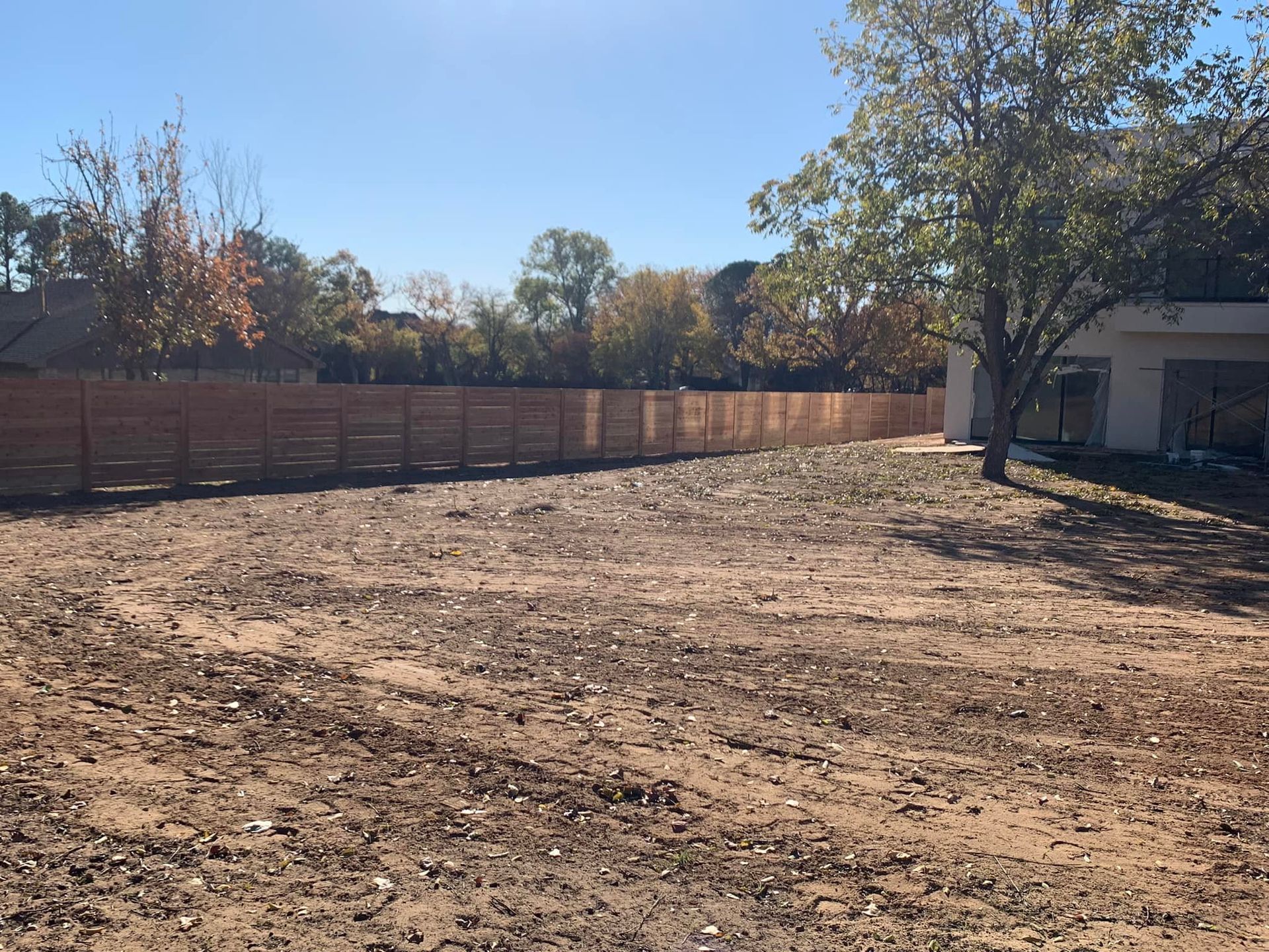 A cleared backyard with a new wooden fence. Trees in the background and a house to the right.