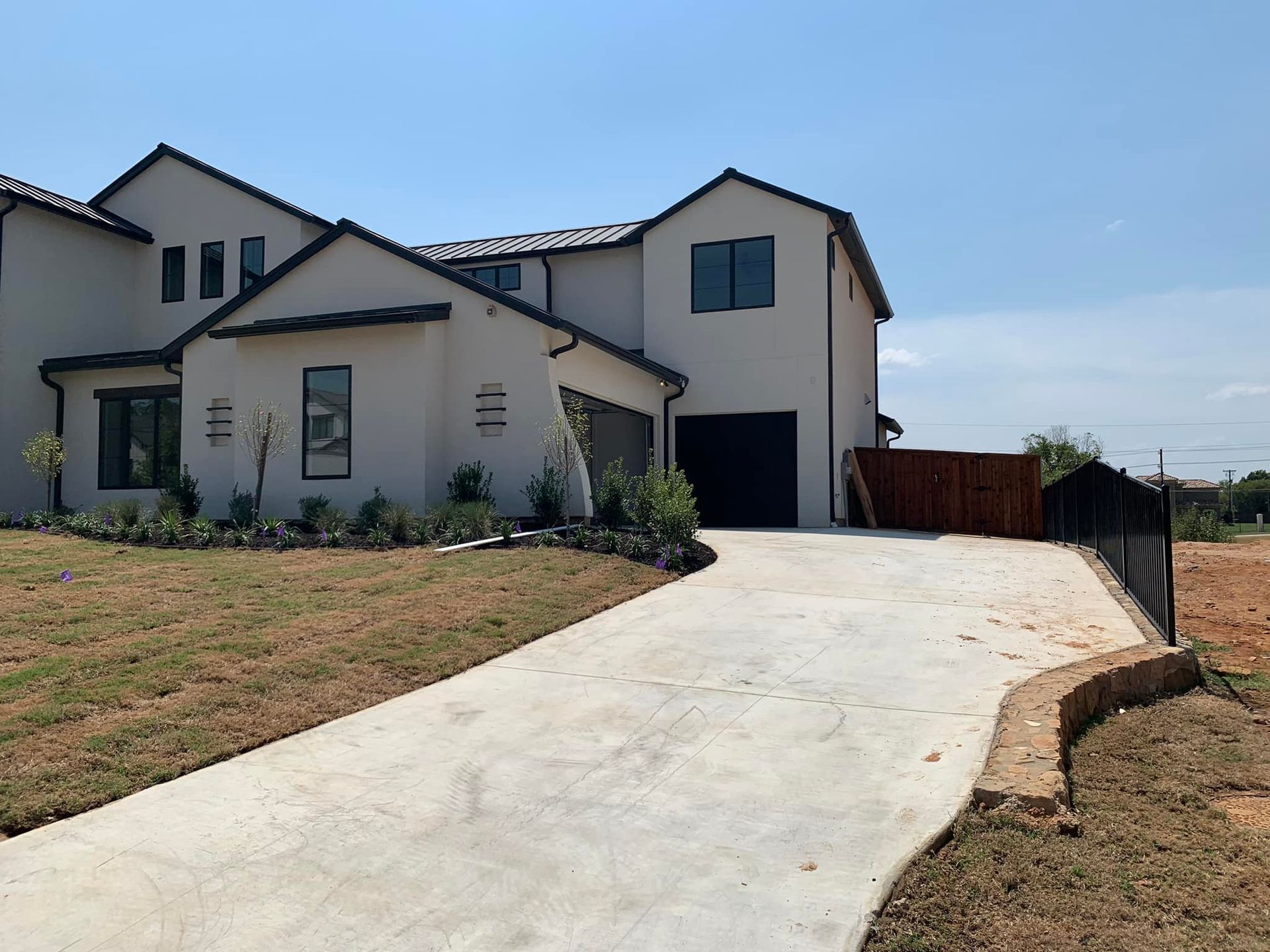 Two-story white house with black trim and garage. Concrete driveway. Dry grass and blue sky.