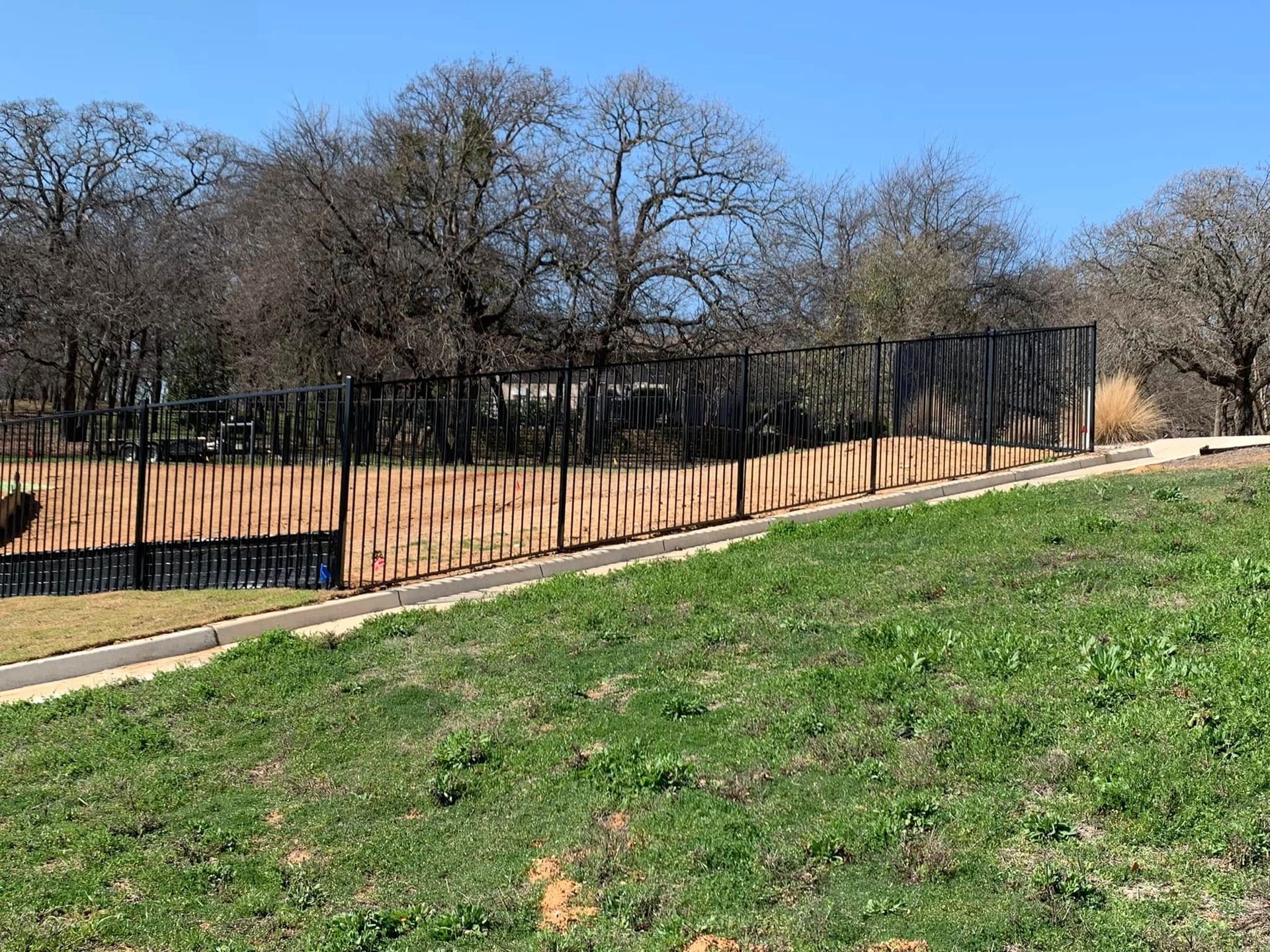 Fence with wood and black metal panels, grassy area, trees in background.