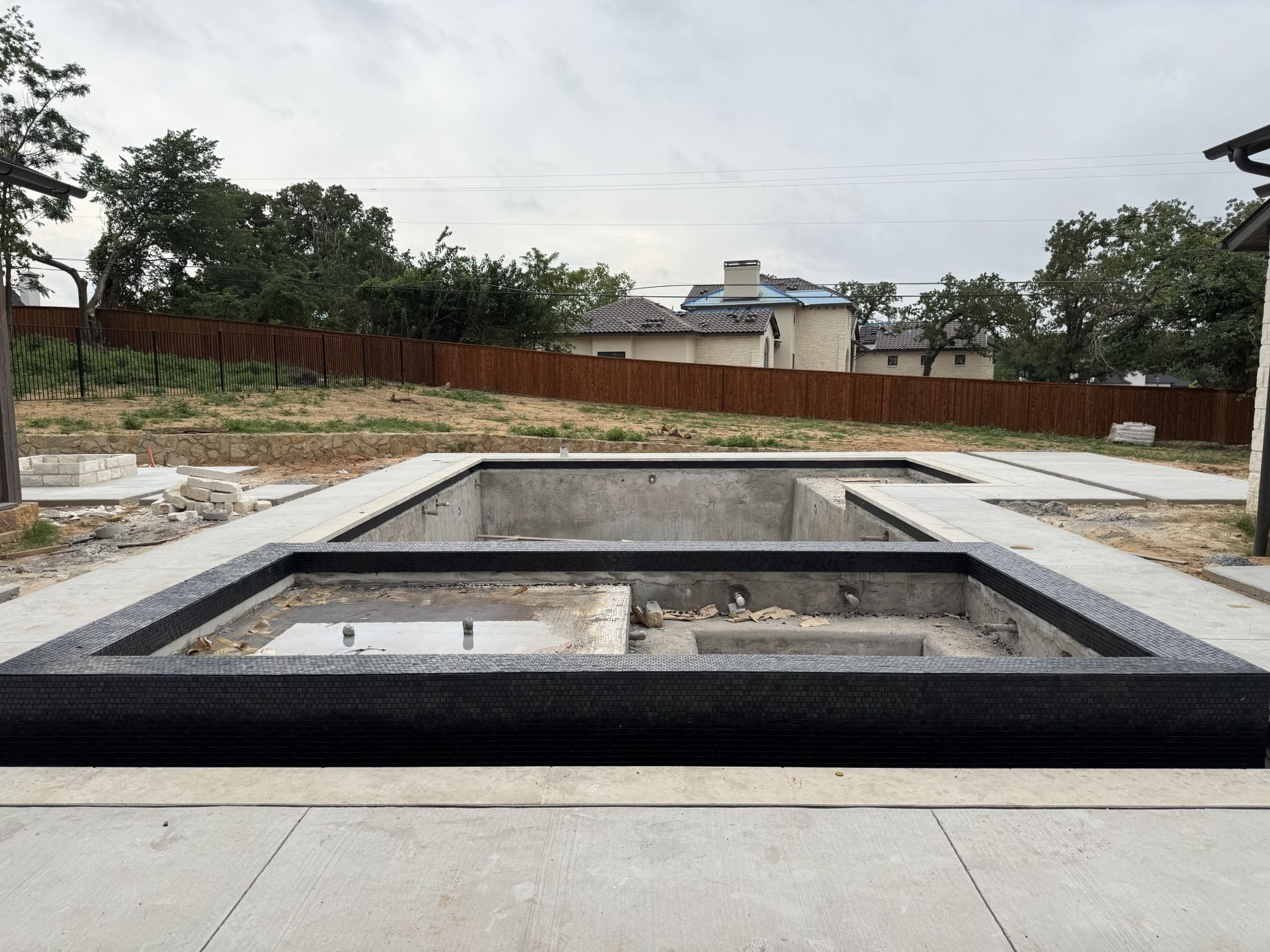 Concrete pool under construction in a backyard. Gray and black rectangular form, surrounded by concrete.