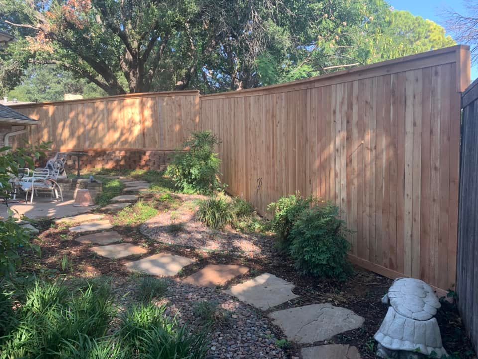 A wooden fence surrounds a backyard garden with stone path, plants, and turtle statue.