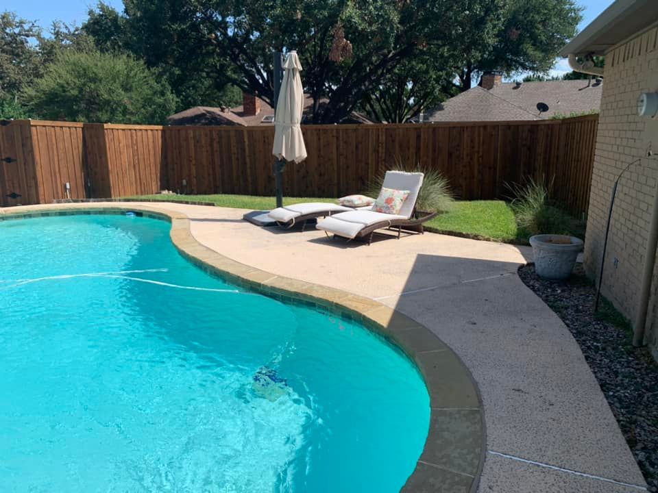 Swimming pool with lounge chairs, umbrella, and a wooden fence.