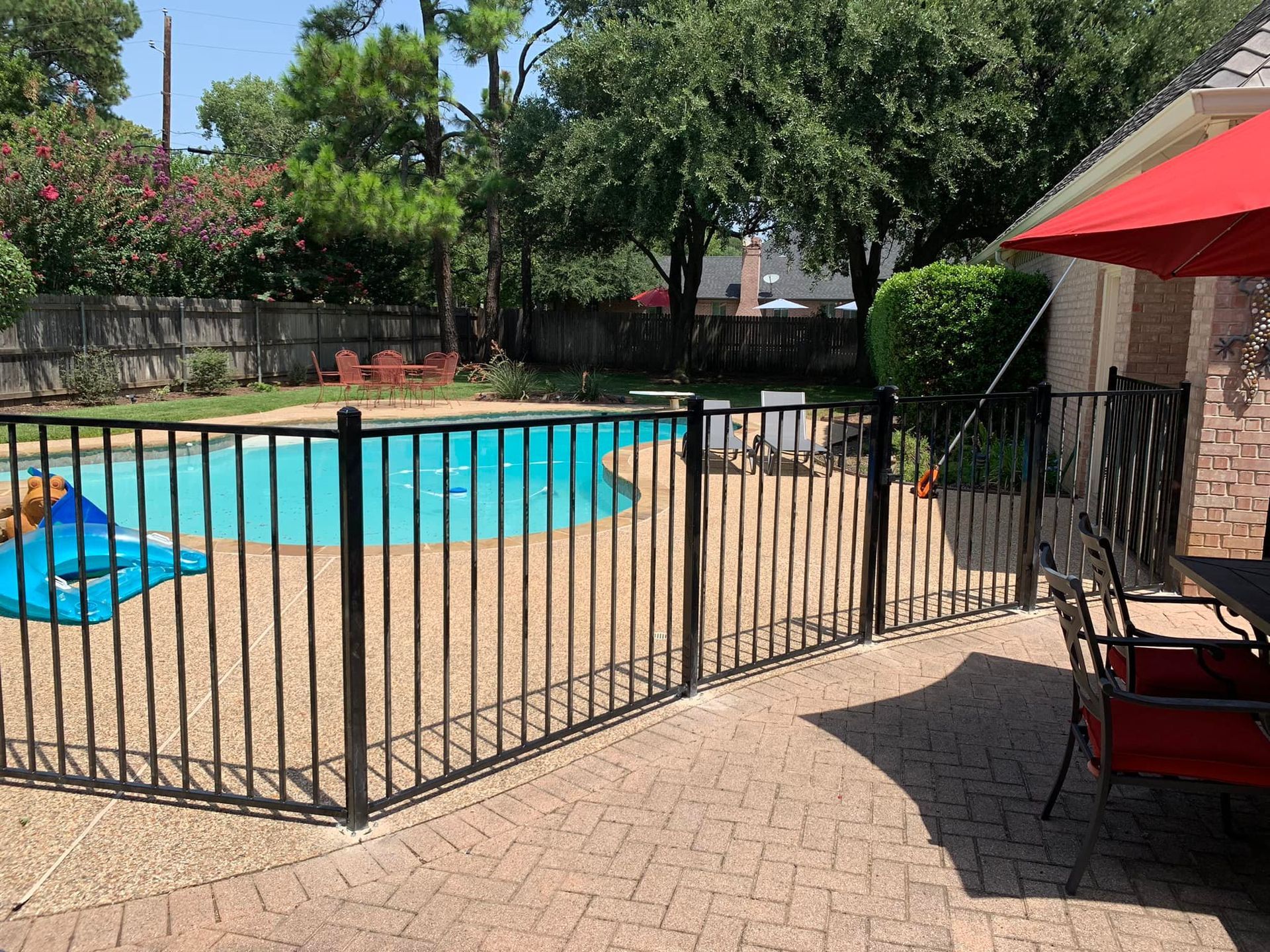 Black fenced pool area with turquoise water. Red umbrella and patio furniture visible.