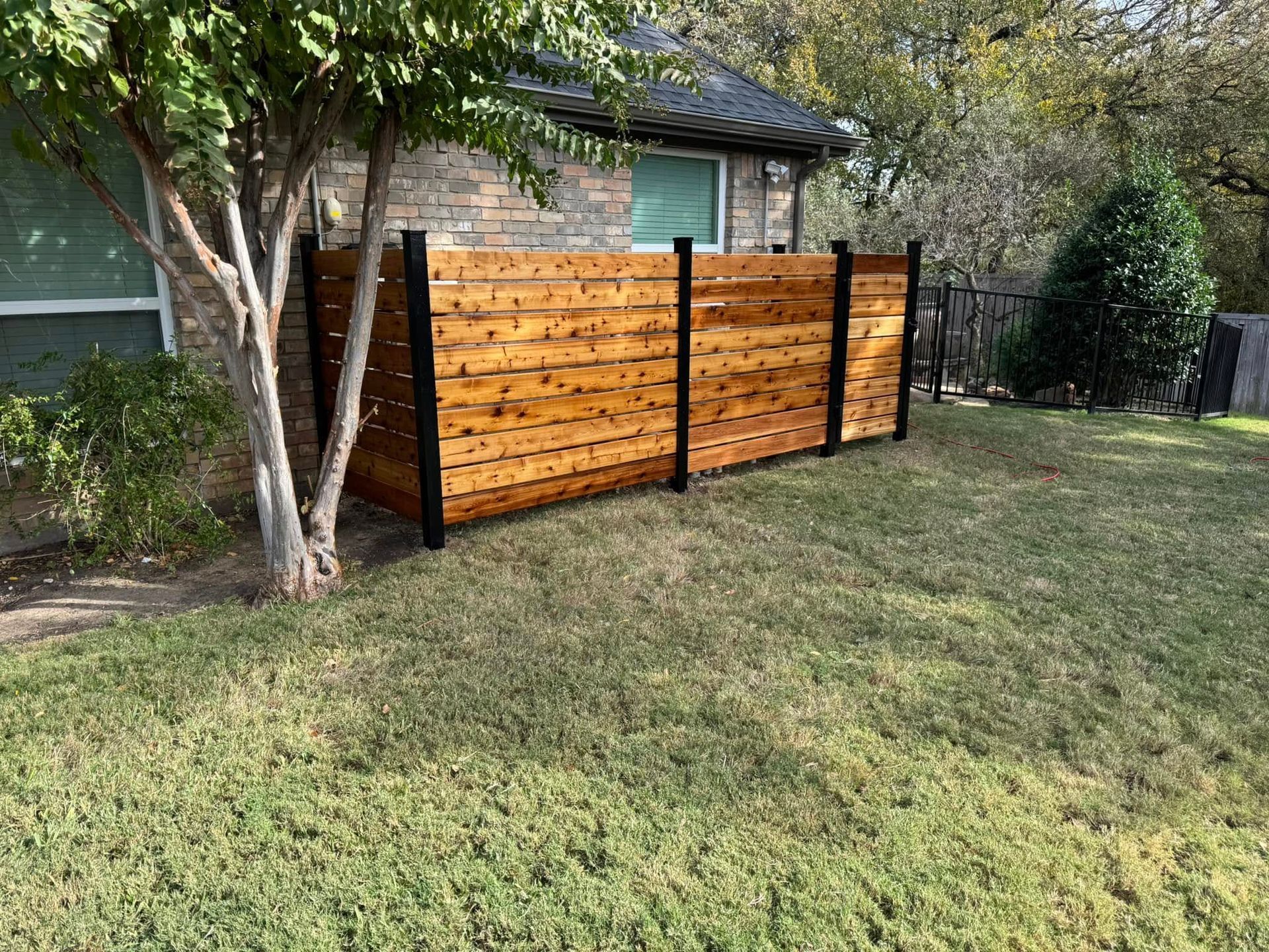 Wooden privacy fence in backyard, next to a house with green grass and trees.