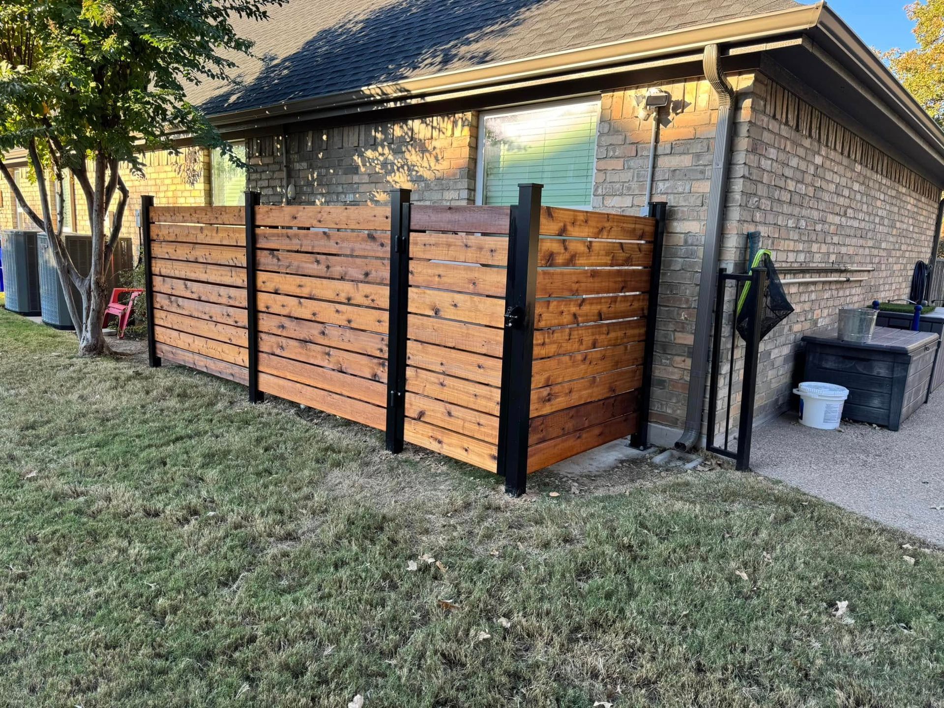 A wooden privacy fence with black posts next to a brick house on a grassy lawn.