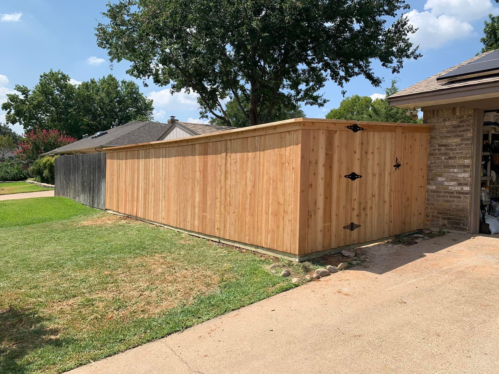 Wooden fence with green lawn, gravel path, and a house.