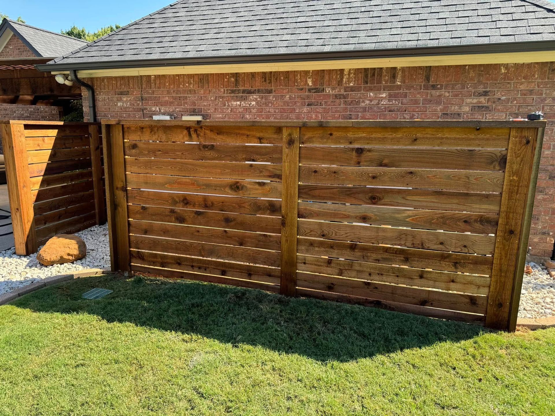 Wooden slatted privacy fence next to a brick building with green grass and gravel below.