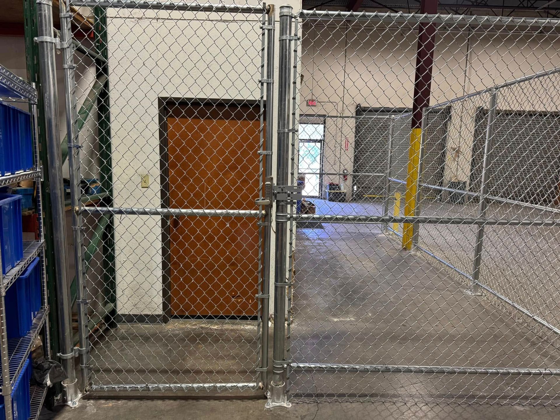 Chain link fence with a gate in front of a brown door inside a warehouse.