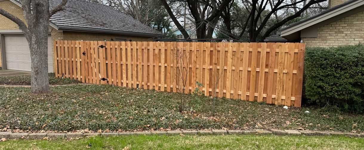 Wooden fence in front of a house. Overgrown shrubbery and tree in the yard.