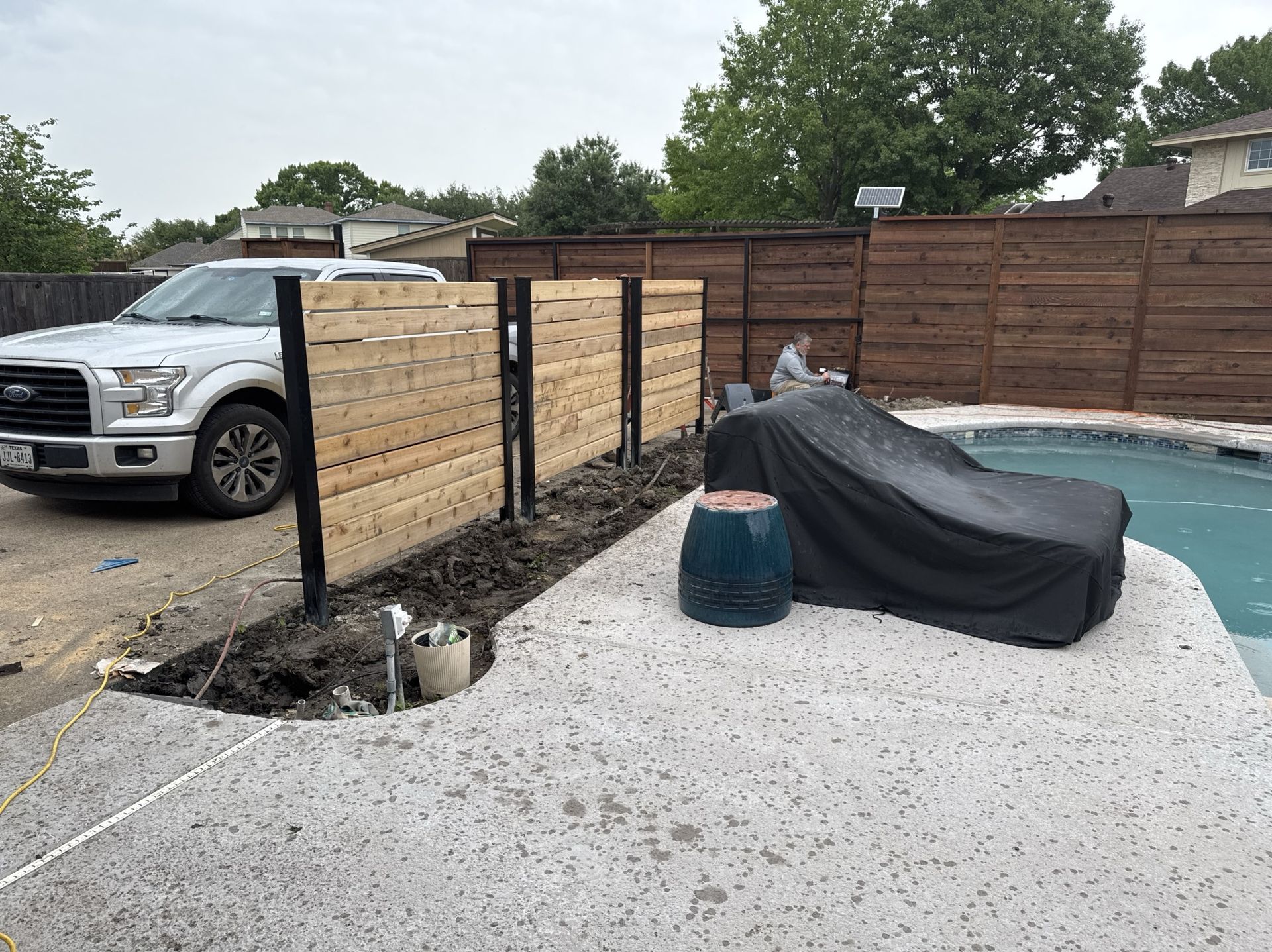 A backyard with a new wooden fence, a pickup truck, and a pool covered in black tarp.