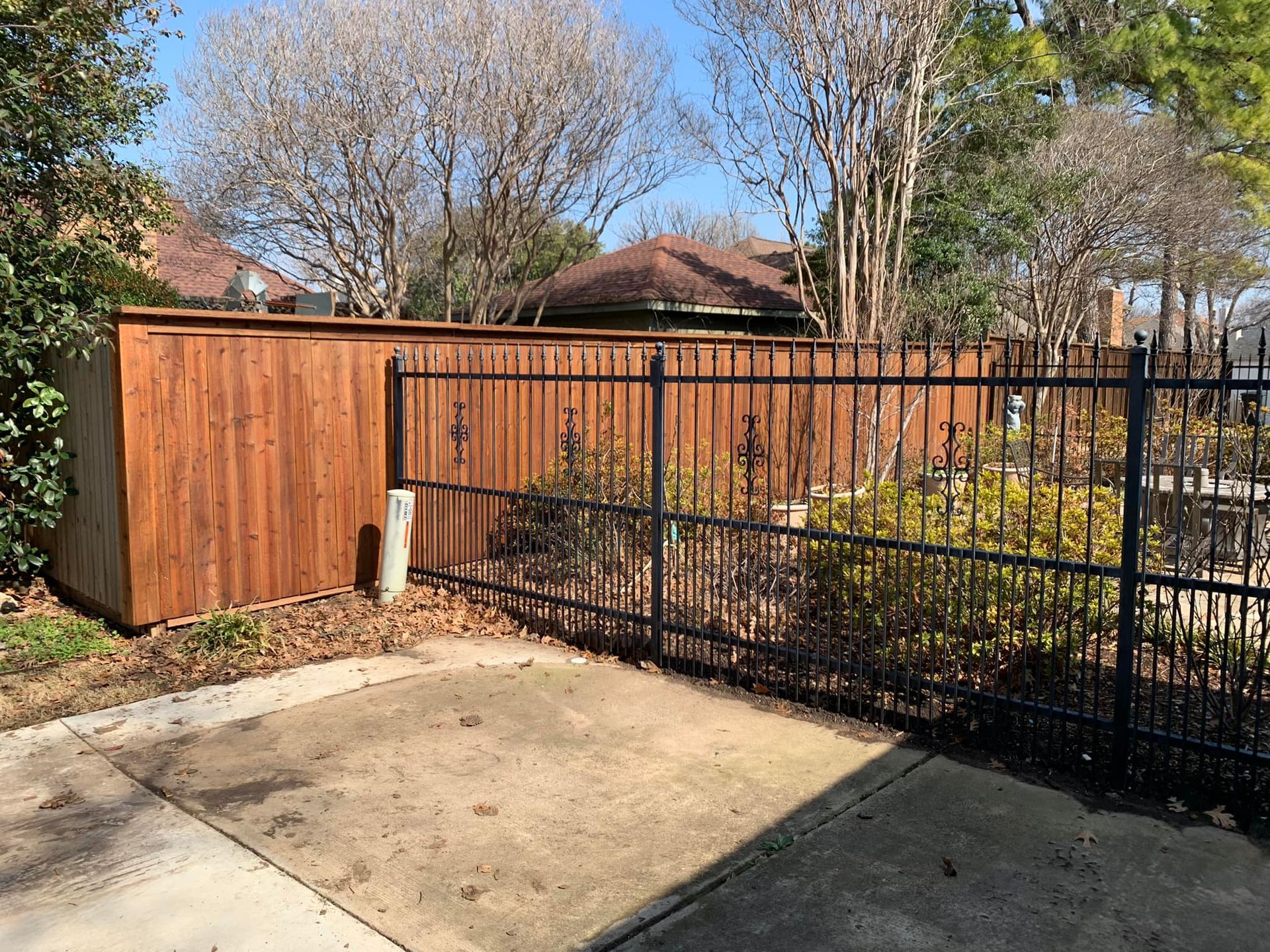 Wooden privacy fence and black wrought-iron fence separate a yard with a patio in front.