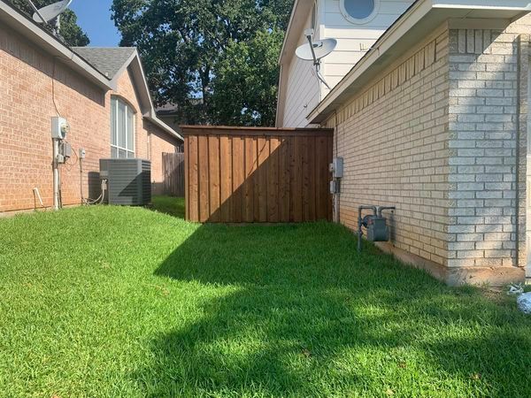 Backyard view between two houses with a wooden fence, green grass, and an AC unit.