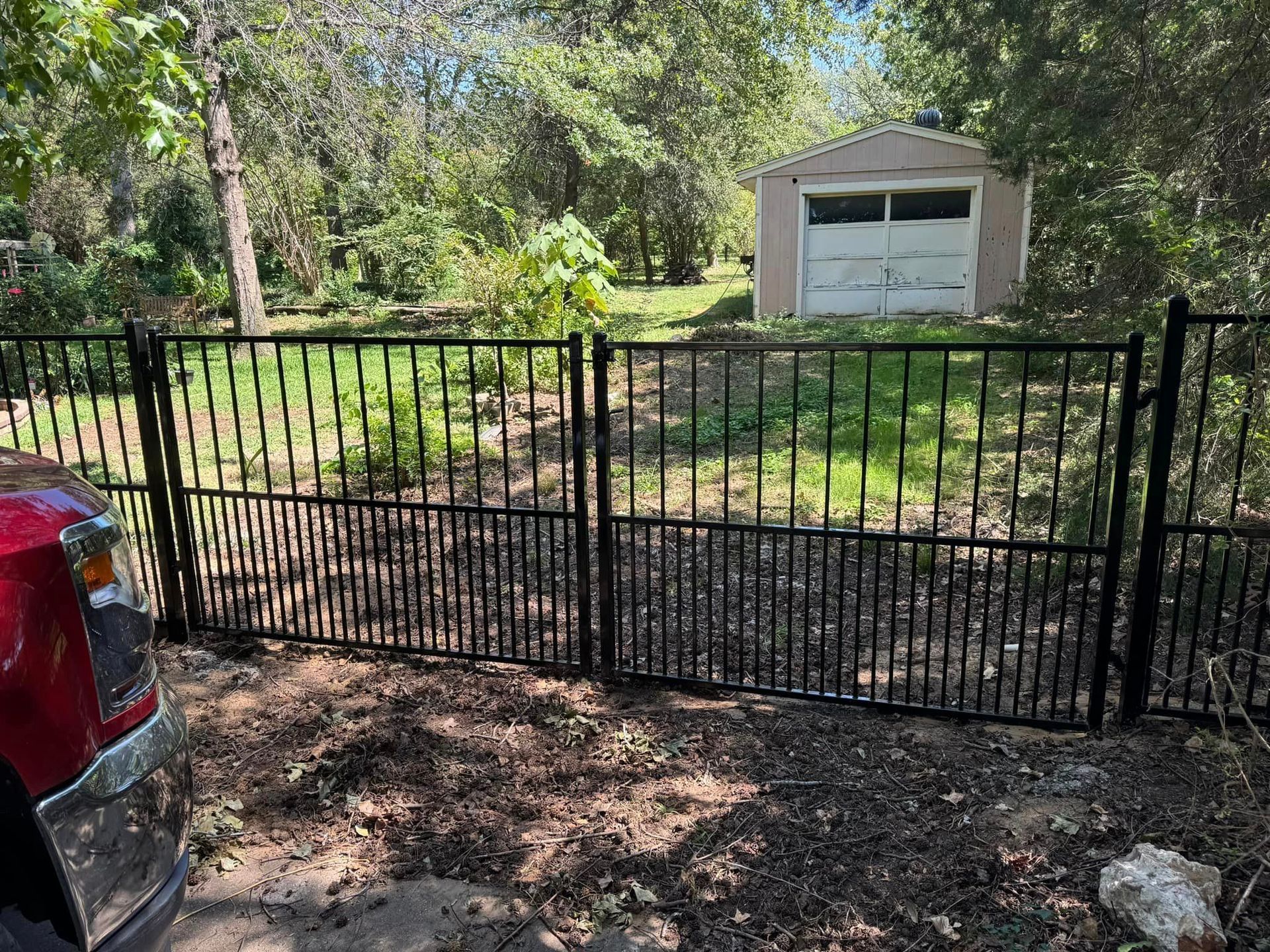 Black metal fence enclosing a yard with a shed in the background; a red vehicle is in the foreground.