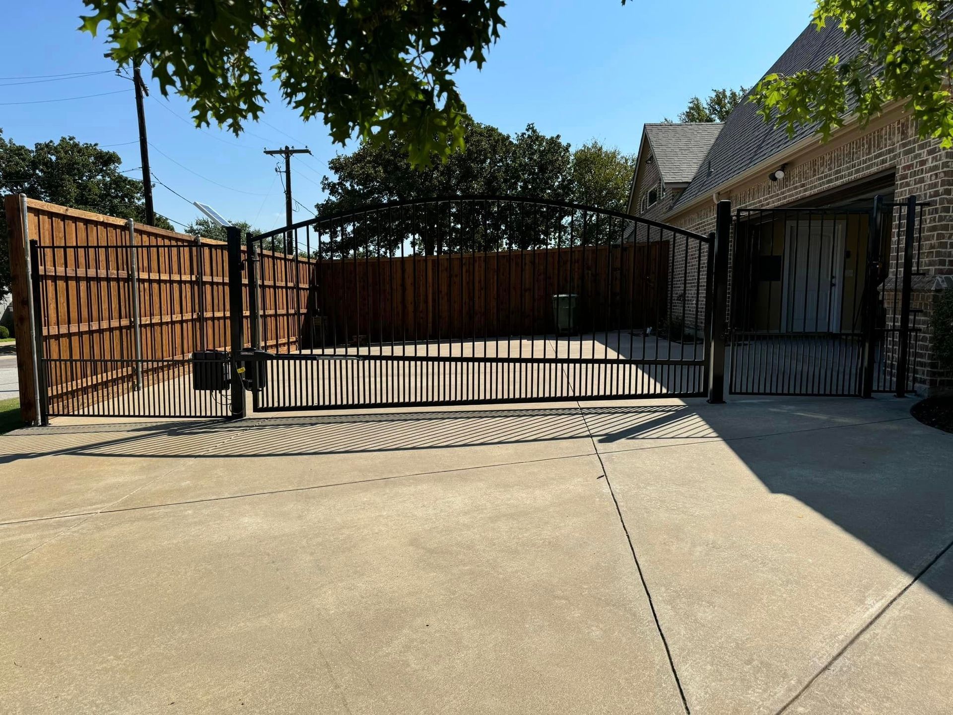 Driveway with brown wooden and black metal gates leading to a house.