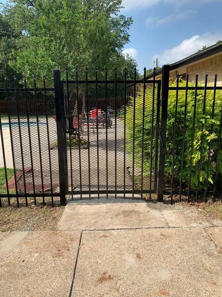 Black metal gate on a concrete walkway, leading to a backyard with a pool.