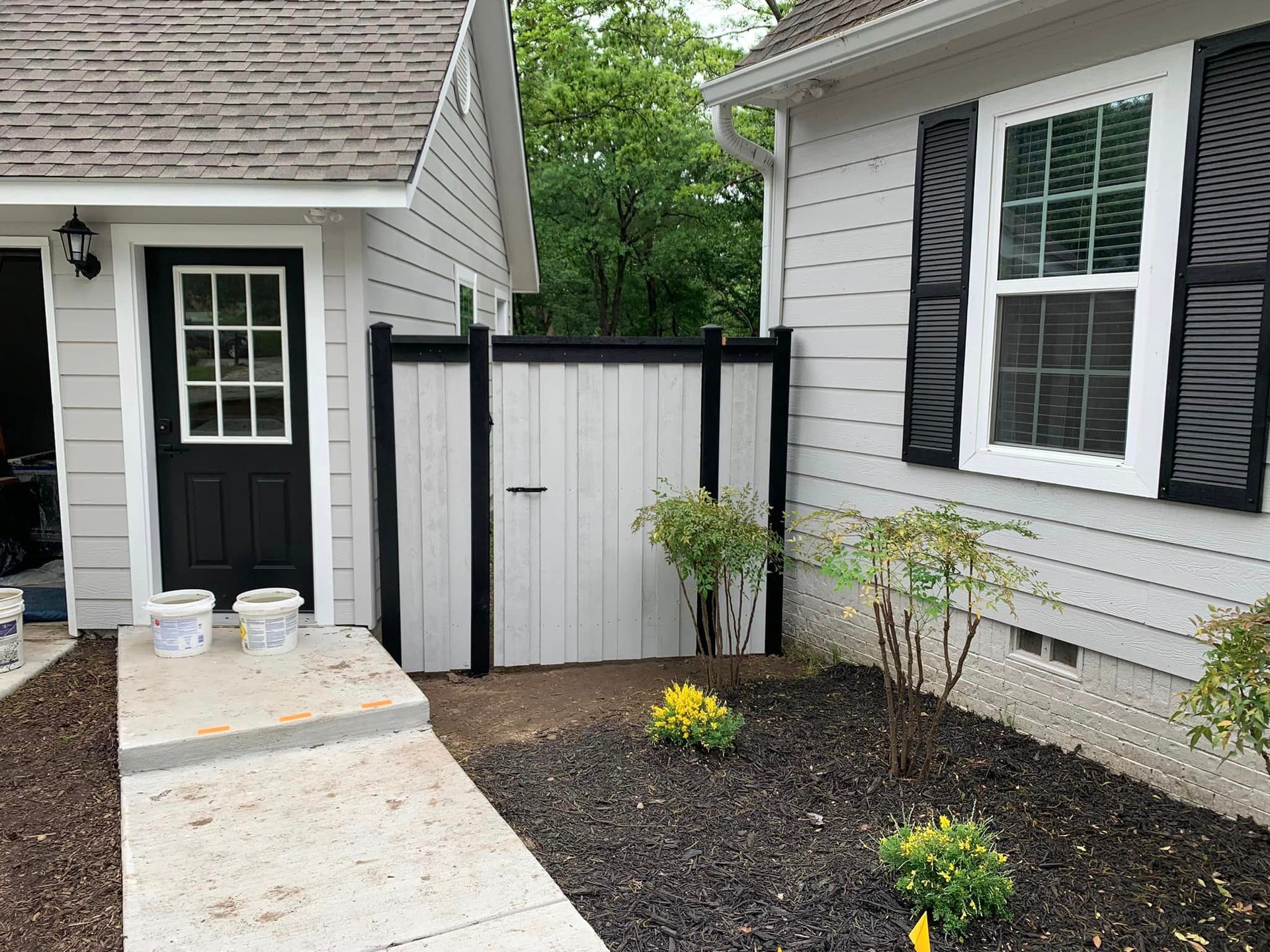 Exterior view: light gray house with black shutter and gate; pathway with flowerbed.