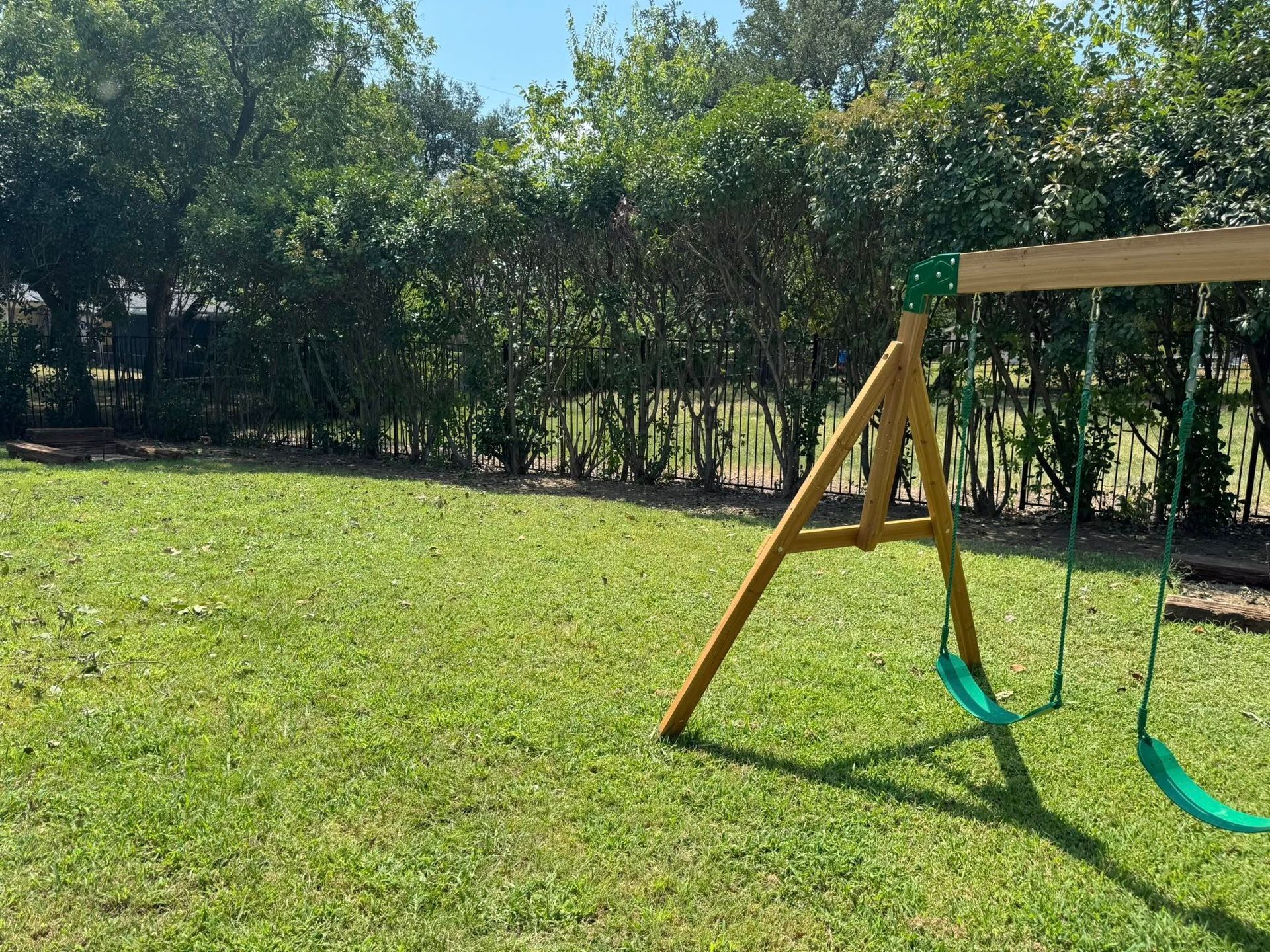 Swing set in a grassy backyard, green trees in the background.