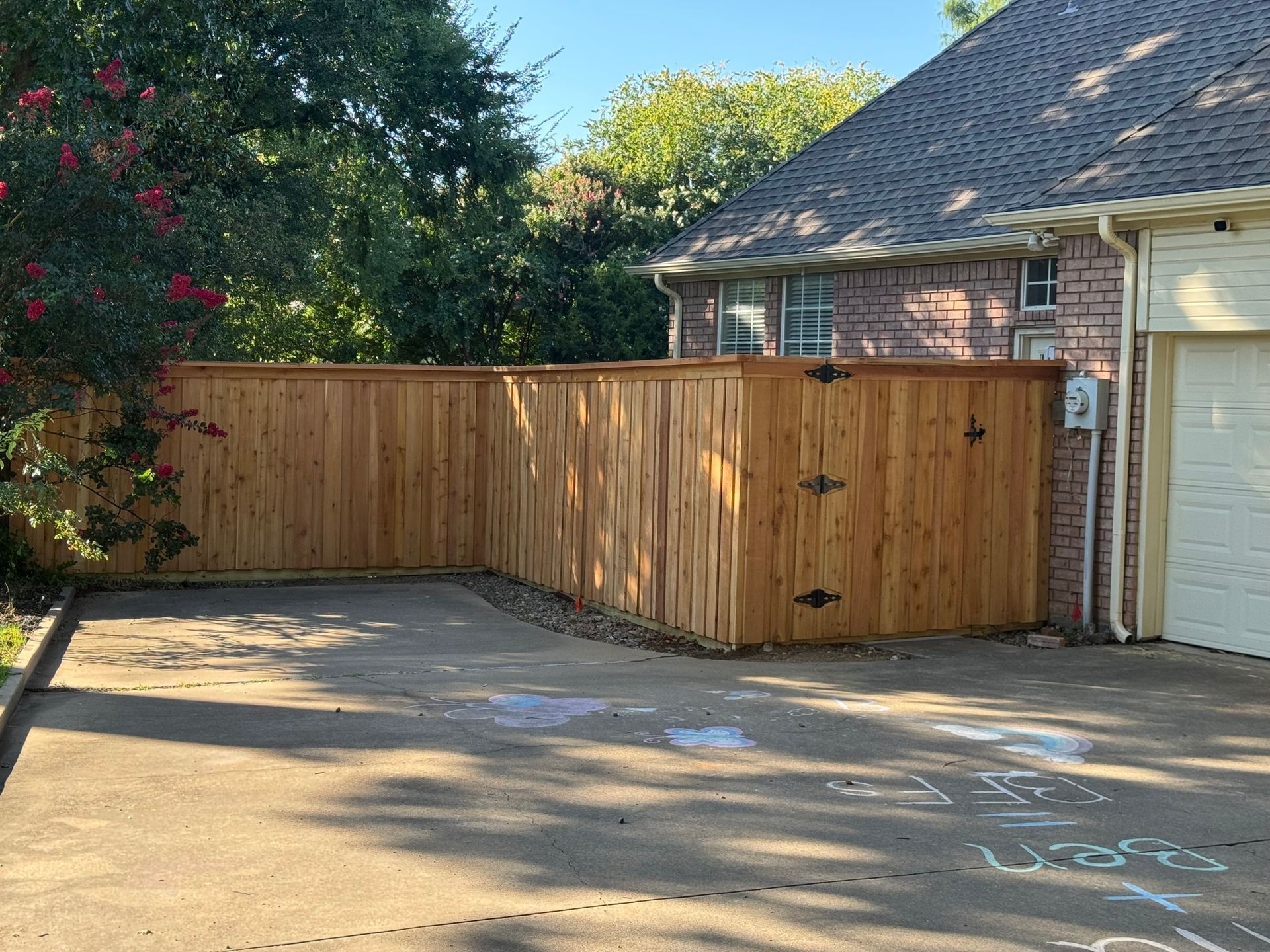 Wooden fence bordering a driveway, next to a brick house and garage.