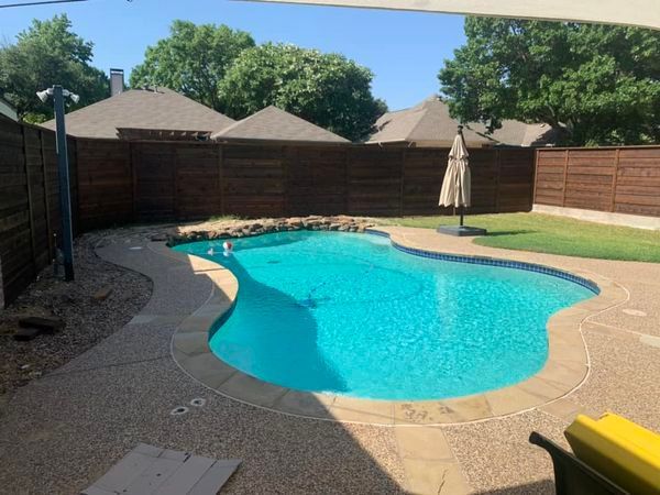 Backyard with swimming pool, brown fence, and umbrella on a sunny day.