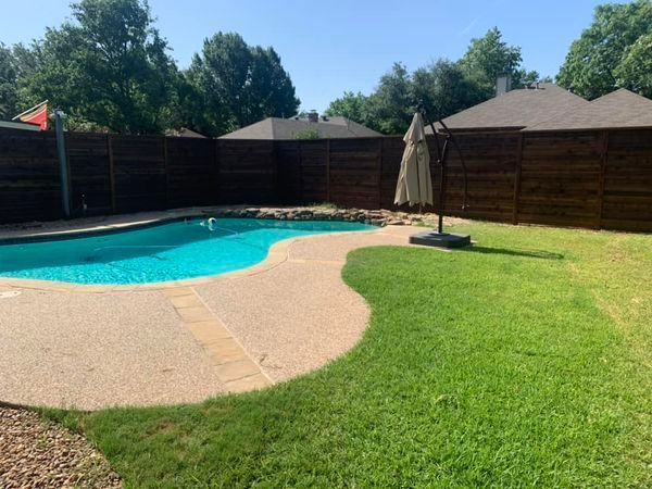 Backyard with a turquoise pool, a patio, green grass, a brown fence, and a closed umbrella.