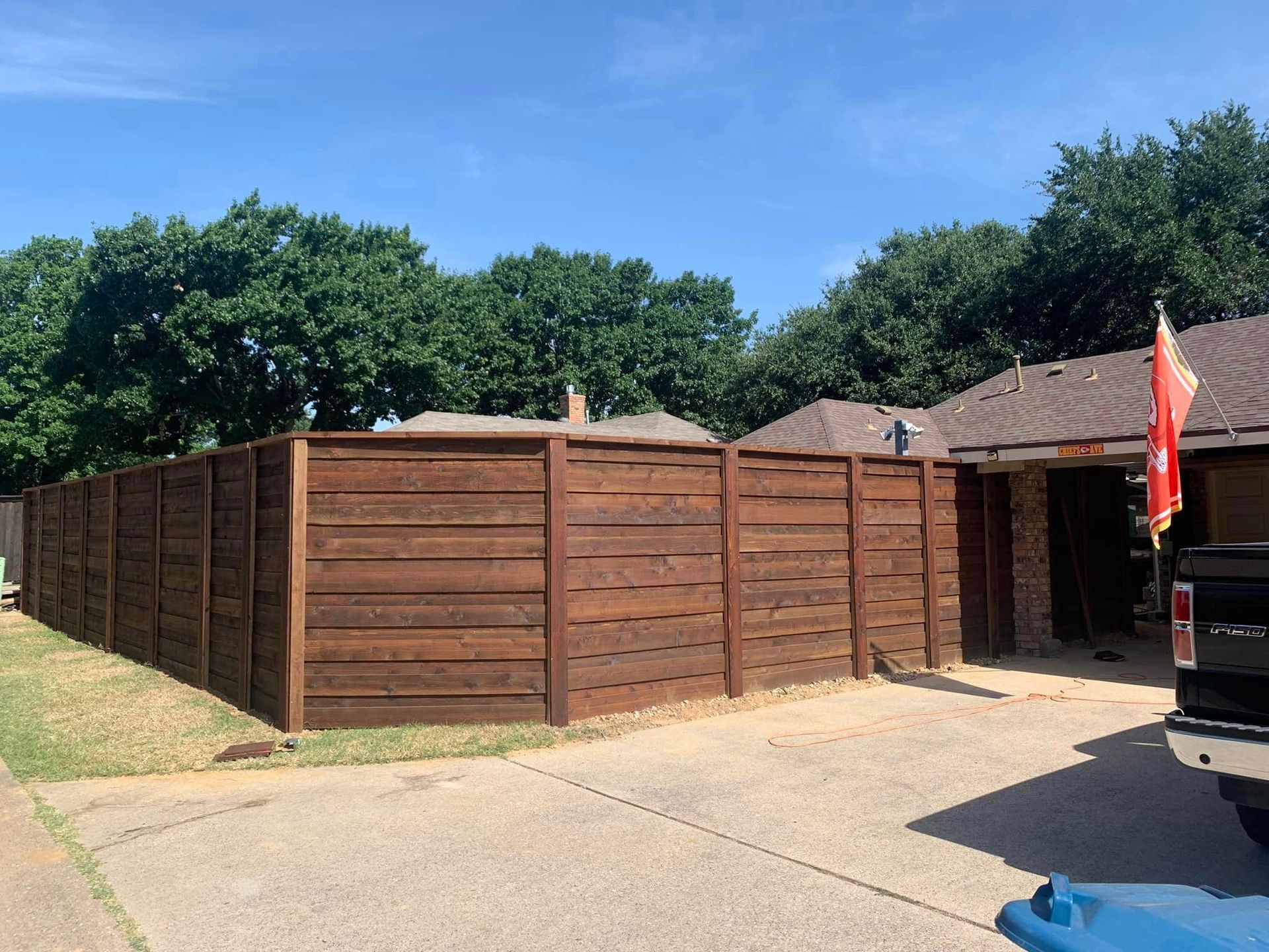 Brown wooden privacy fence surrounding a house with a blue sky.