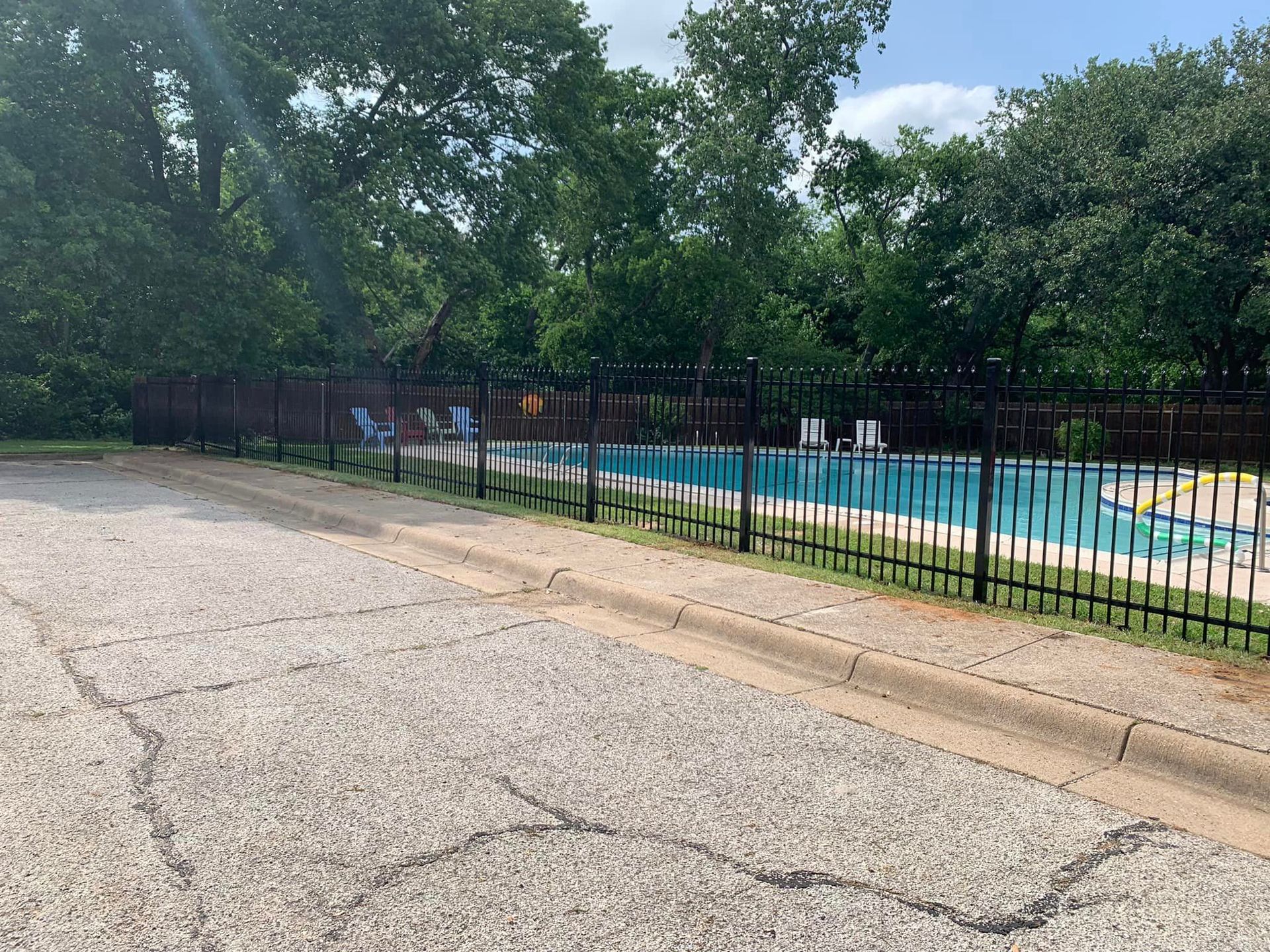A swimming pool with a black fence and trees. The pool is blue.