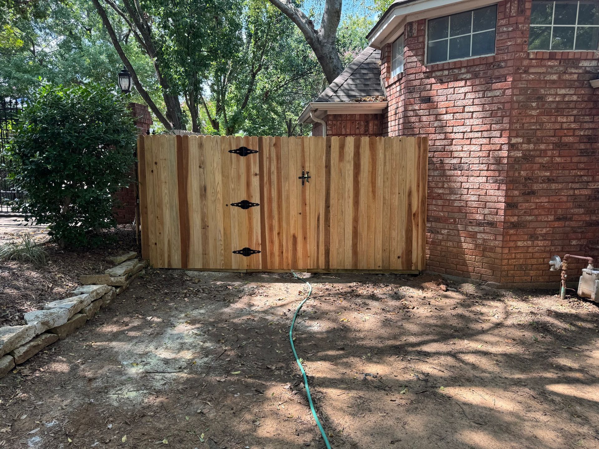 Wooden gate in front of a brick house. It has black hinges and a latch.