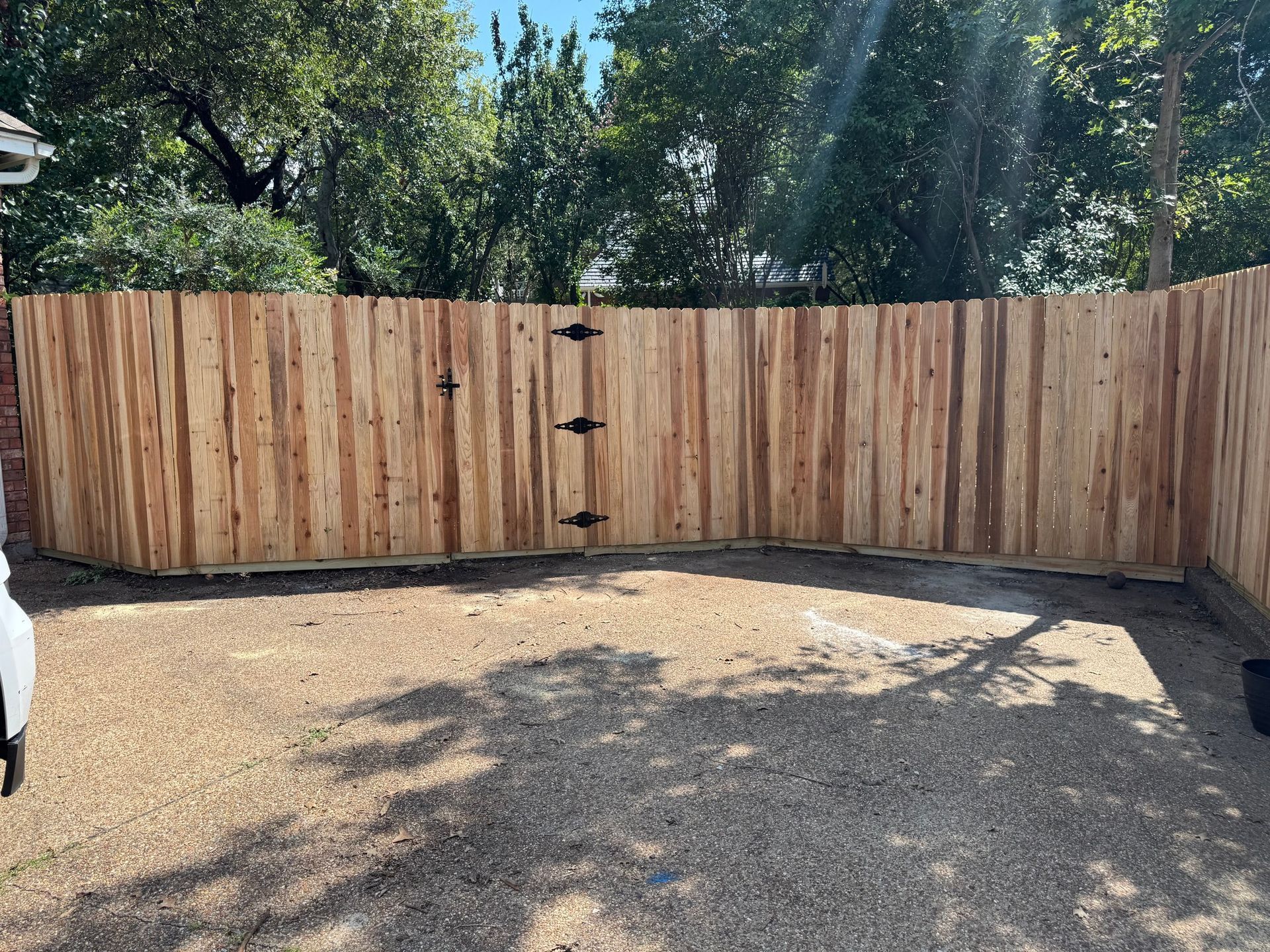 Wooden fence with a gate in front of a gravel driveway.