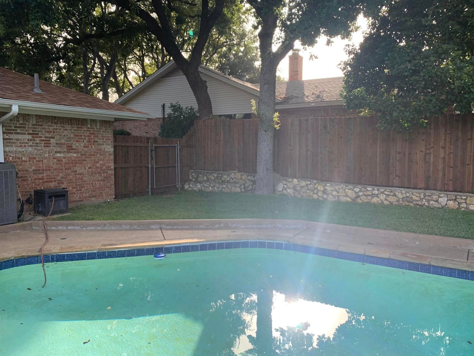 Backyard with a pool, wooden fence, brick wall, and trees.
