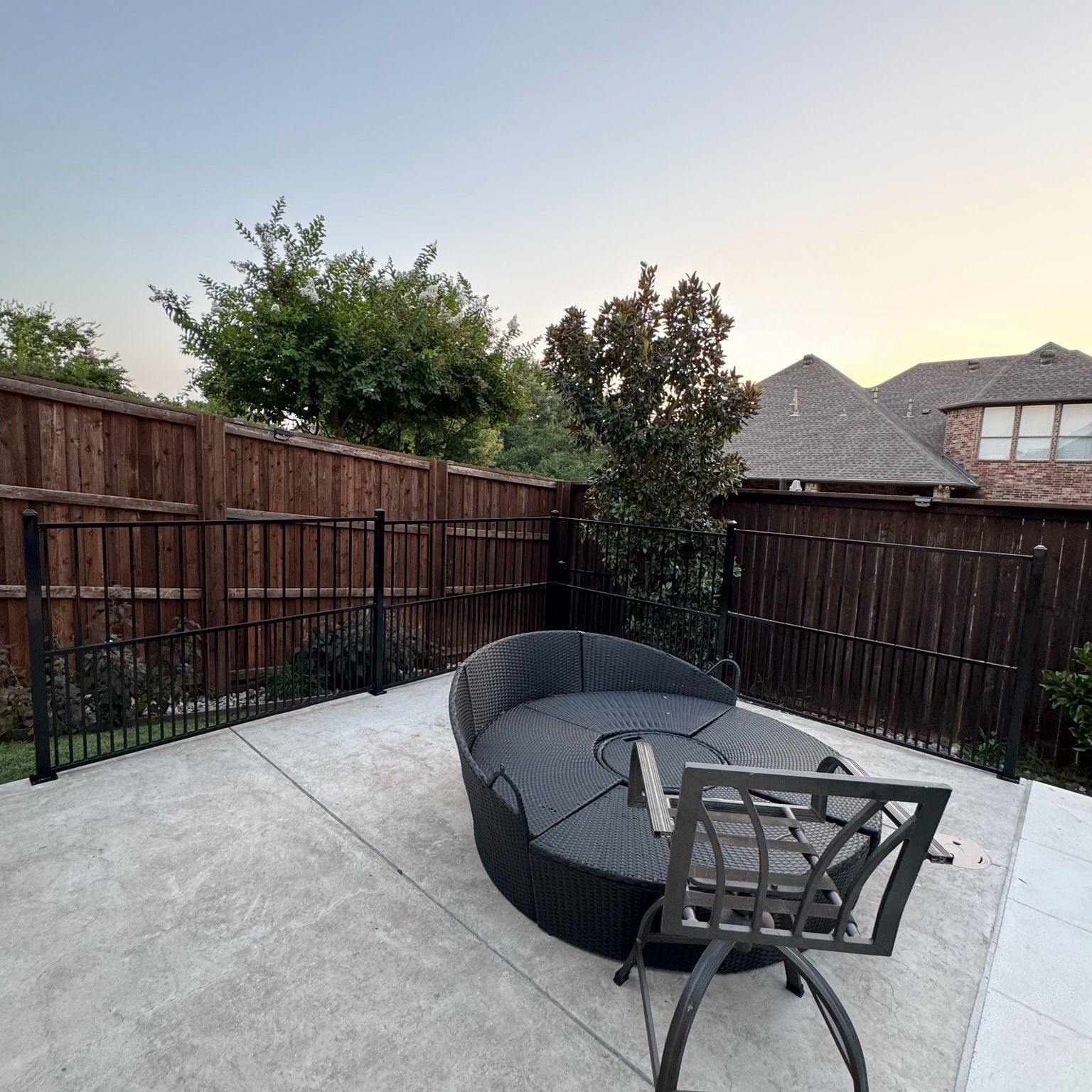Patio with a large black sofa, table, and brown fence. Trees and house in the background.