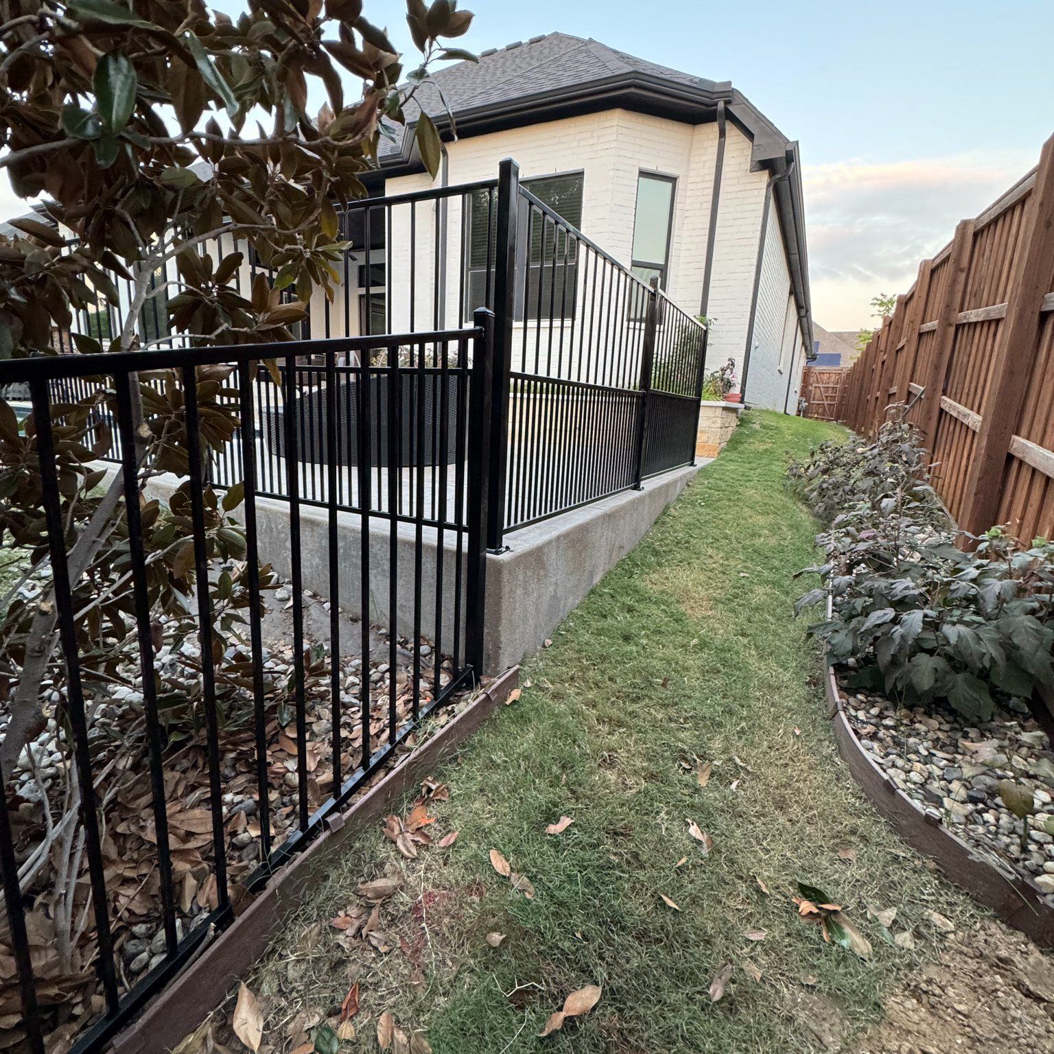 Black fence surrounds a patio next to a house with brick siding and a small green yard.