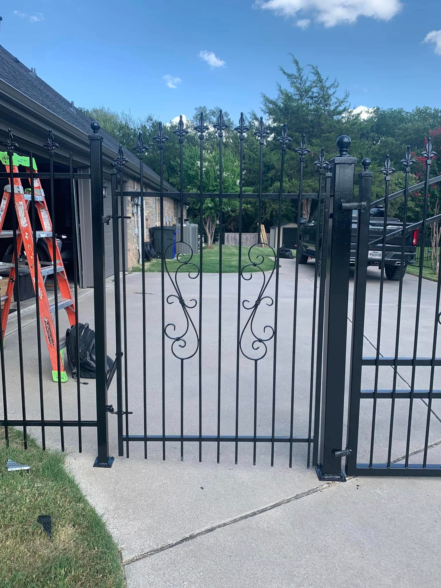 Black metal gate with decorative scrollwork, set in concrete driveway.
