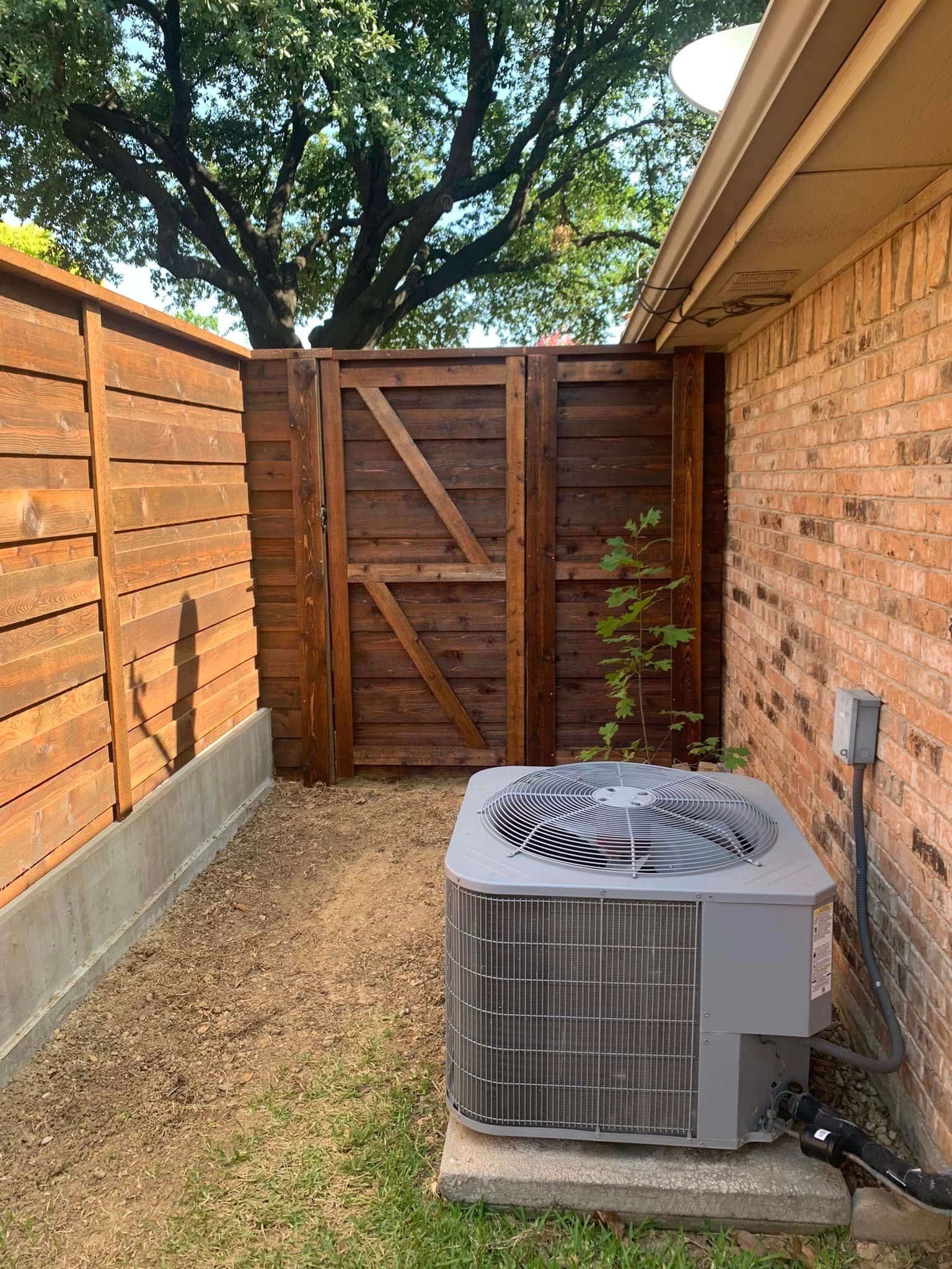 A backyard with a brown wooden fence and gate, air conditioner, and brick wall.