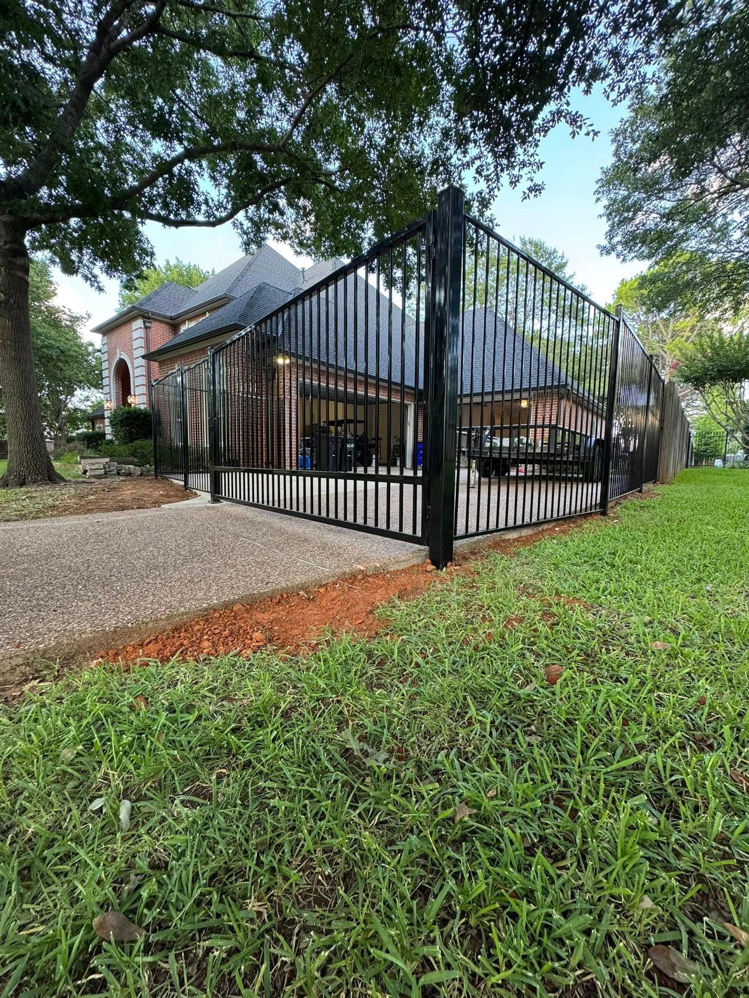 Black iron fence surrounds a home with a brick facade, set on a green lawn under a cloudy sky.