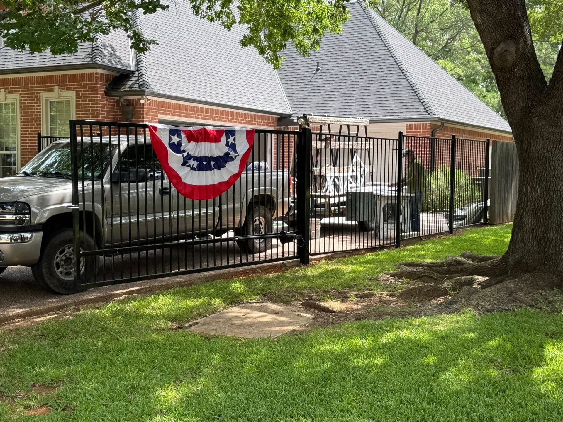 Black metal fence around a yard, truck parked inside, red, white, and blue bunting, person in the yard.