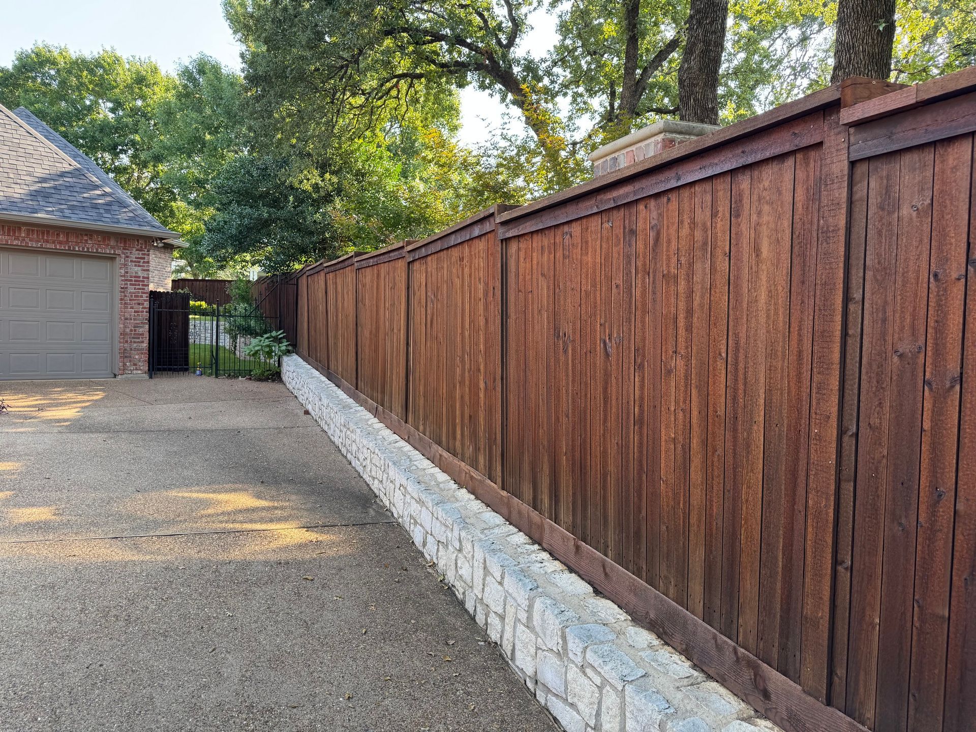 Brown wooden fence atop a stone wall, bordering a gravel driveway.