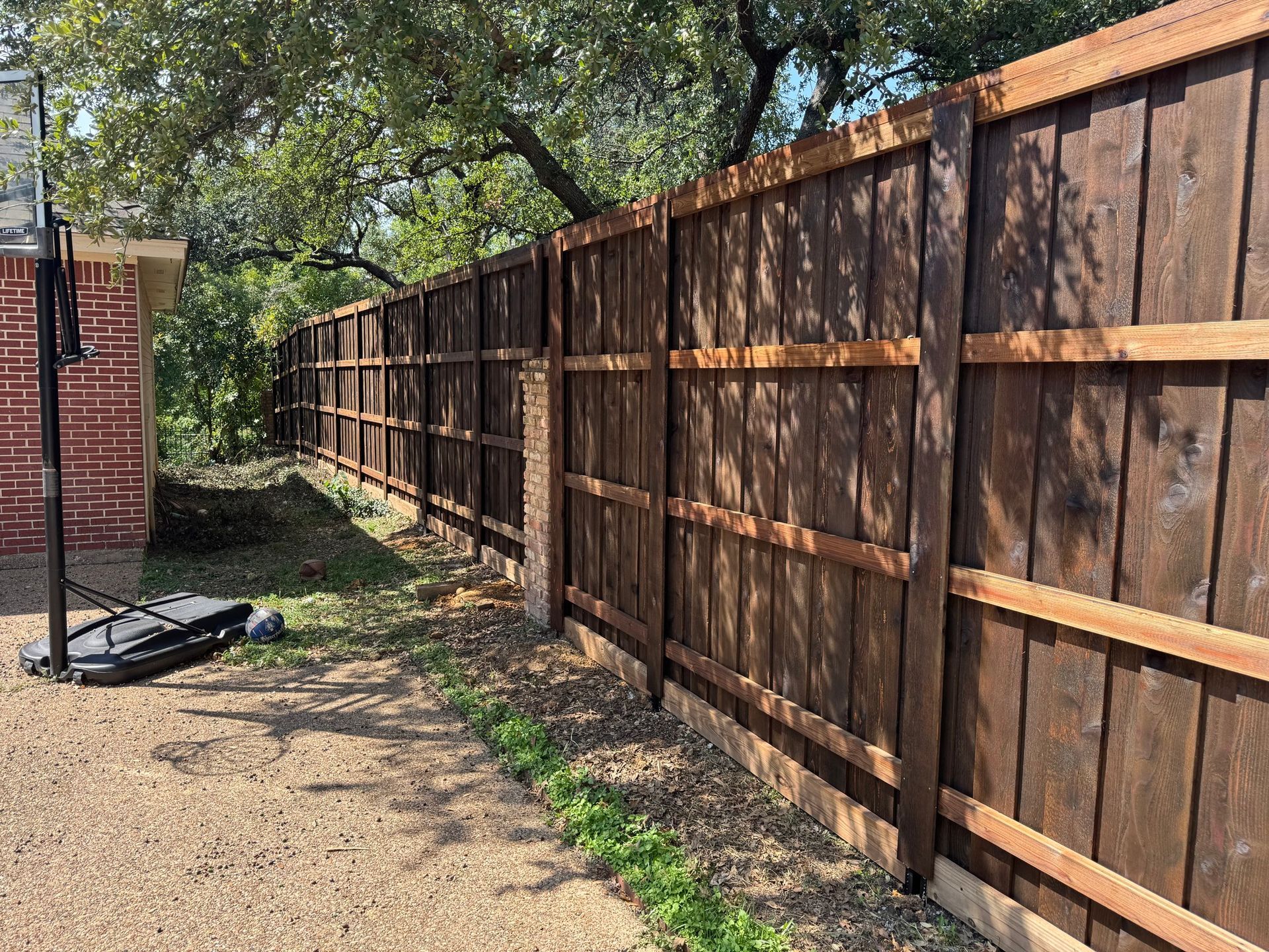 Wooden fence in a backyard, stained brown with a basketball hoop visible.