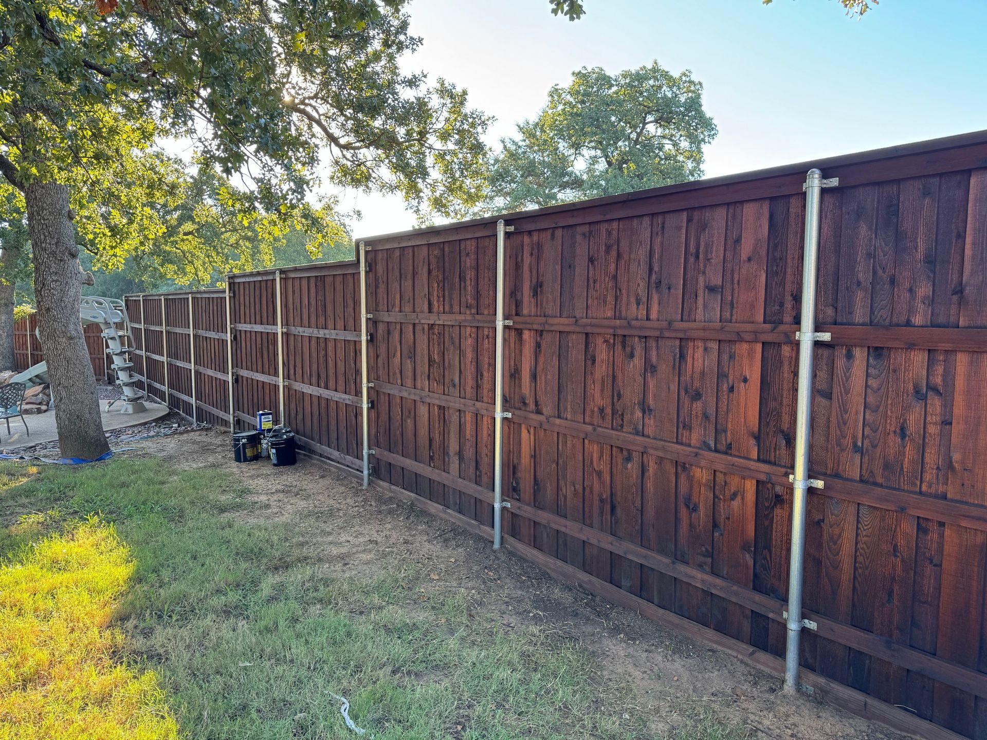 Brown stained wooden fence with silver posts in a grassy yard.