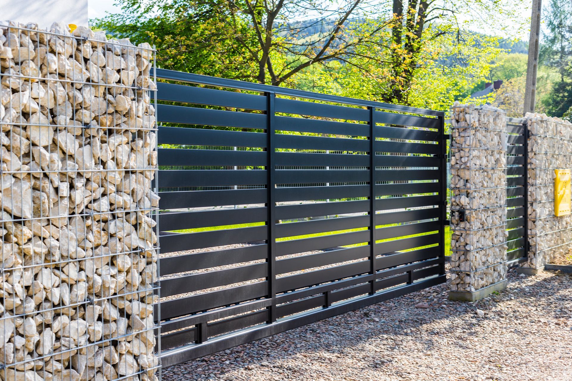 A black sliding gate is surrounded by a stone wall.