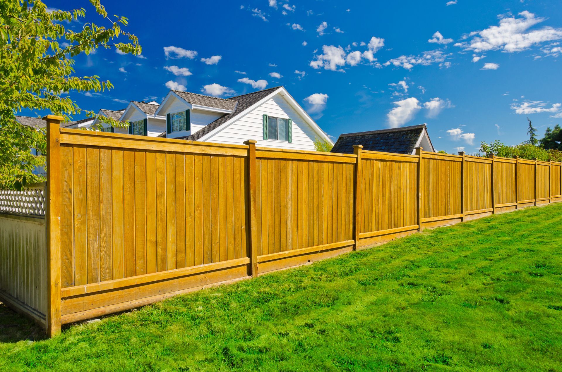 Wooden fence in front of a house with a green lawn and a blue sky.