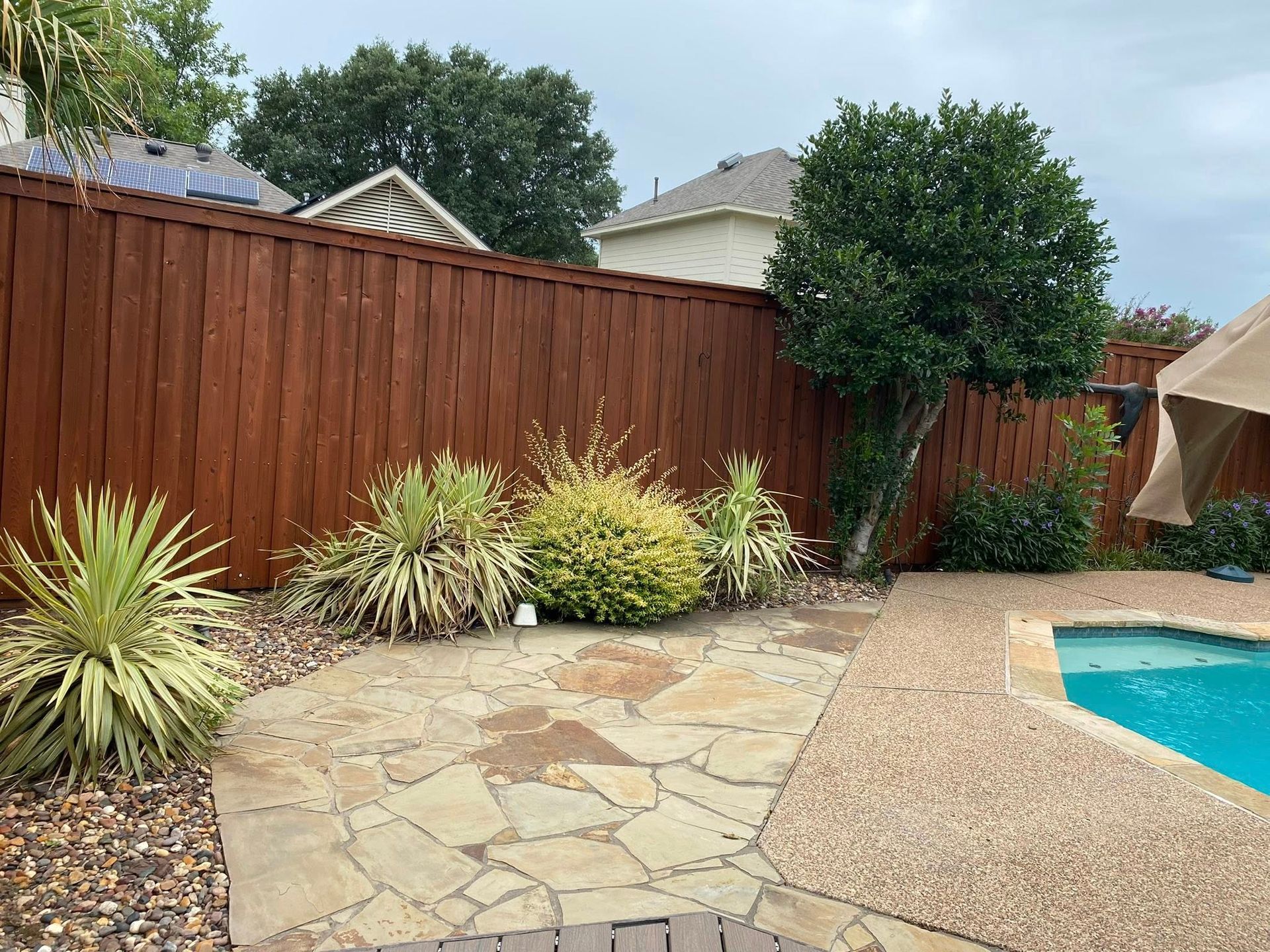 Backyard with pool, stone patio, wooden fence, and landscaping.