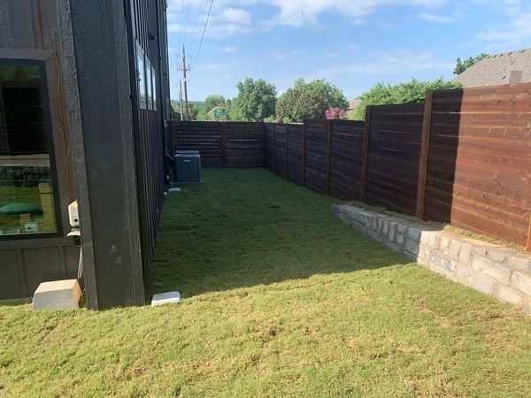 Green backyard with brown wooden fence, grass, and modern house.