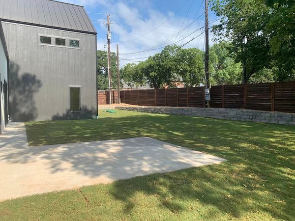 Exterior view of a modern home with gray siding, green grass lawn, and a wooden fence on a sunny day.