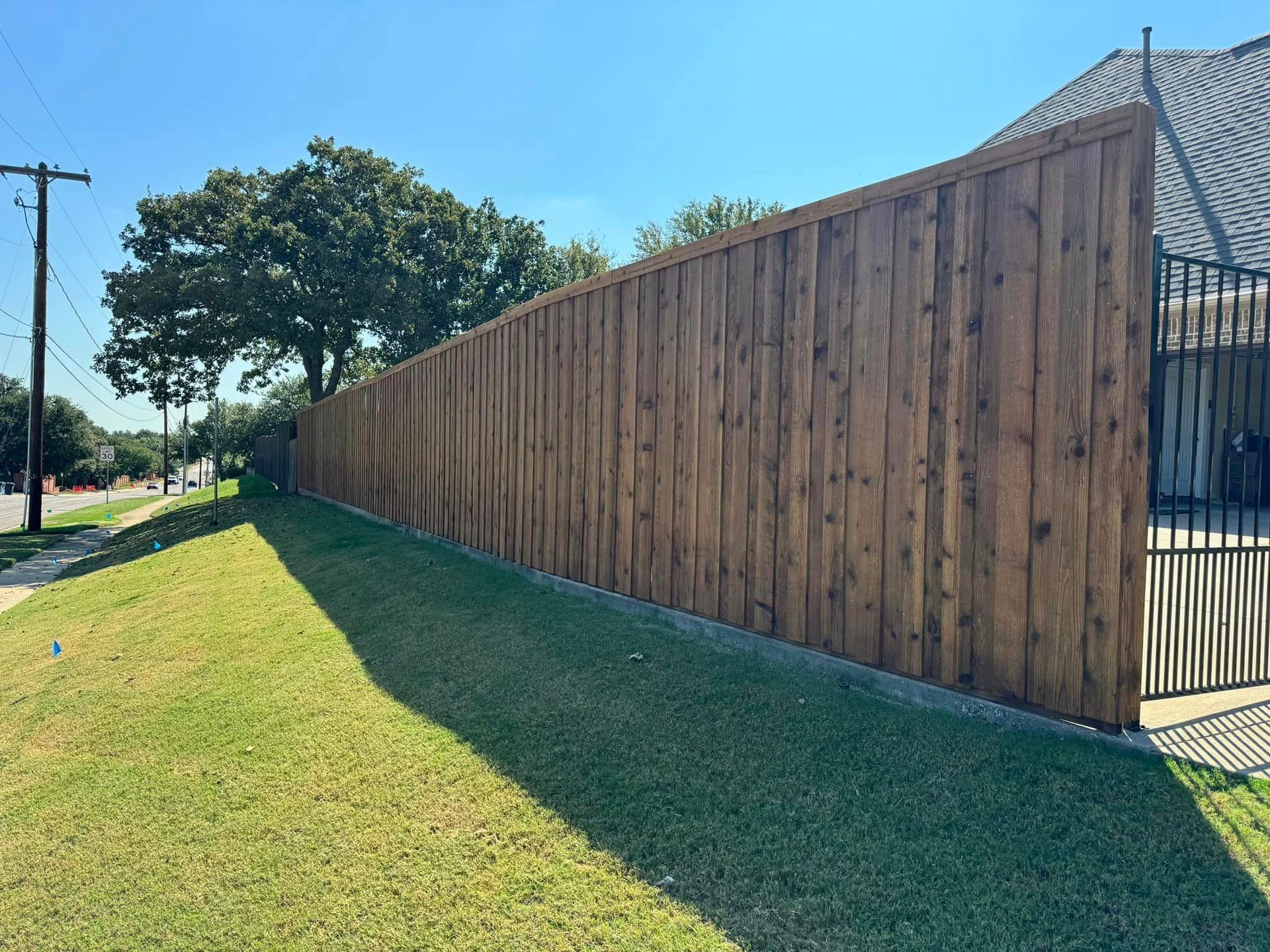 Long, stained wooden fence along a green grassy lawn, under a blue sky.