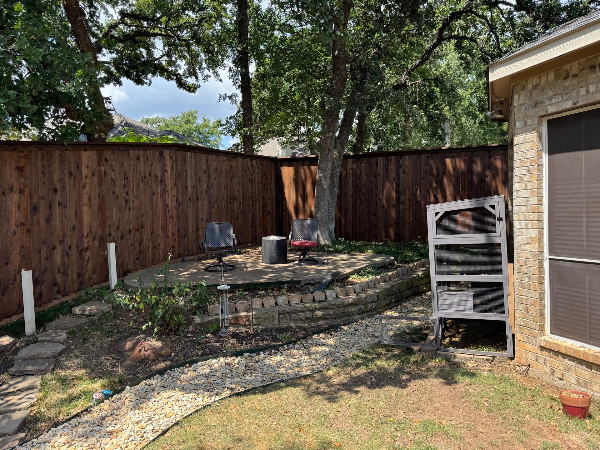Backyard with a brown wooden fence, a tree, chairs, and a small rock garden.