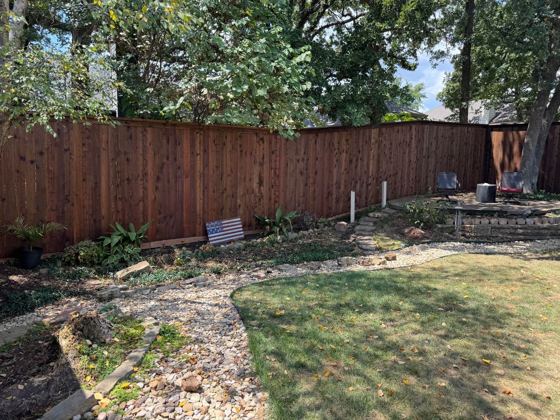 Brown wooden fence in a backyard with a grassy area, plants, and a flag.