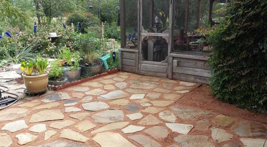 A stone patio with a screen house, potted plants, and a garden in the background.