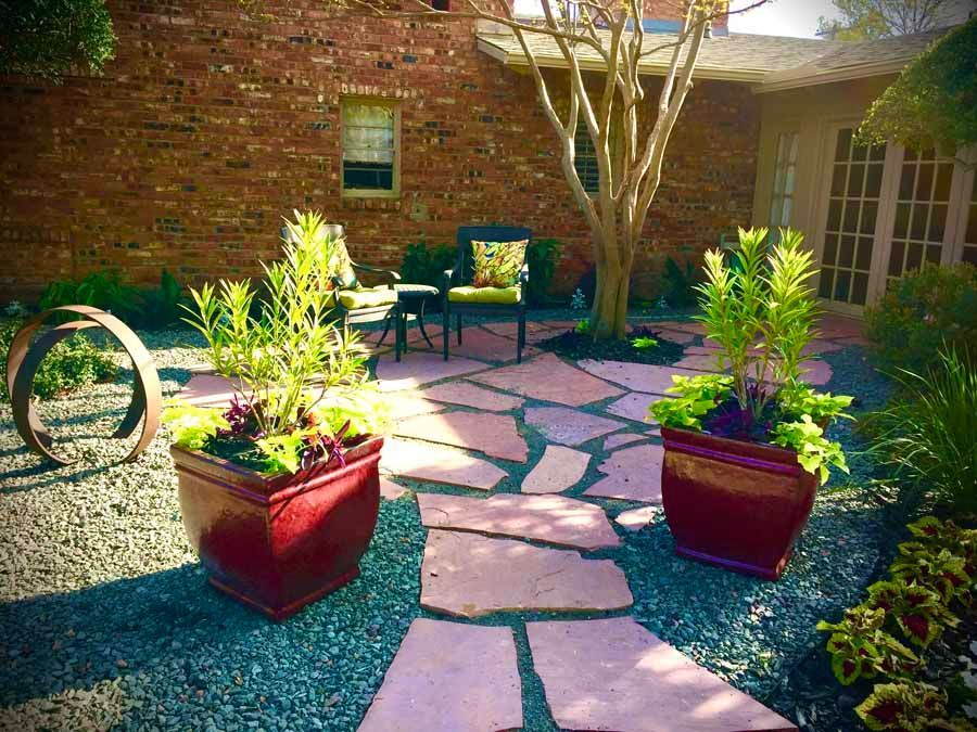 A patio with pink stone pavers, two large red planters, and a small sitting area against a red brick house.