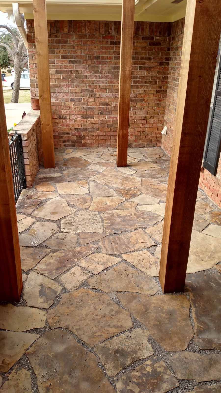 A stone-paved porch area featuring irregular flagstones in shades of tan and brown, framed by brown wooden support posts.